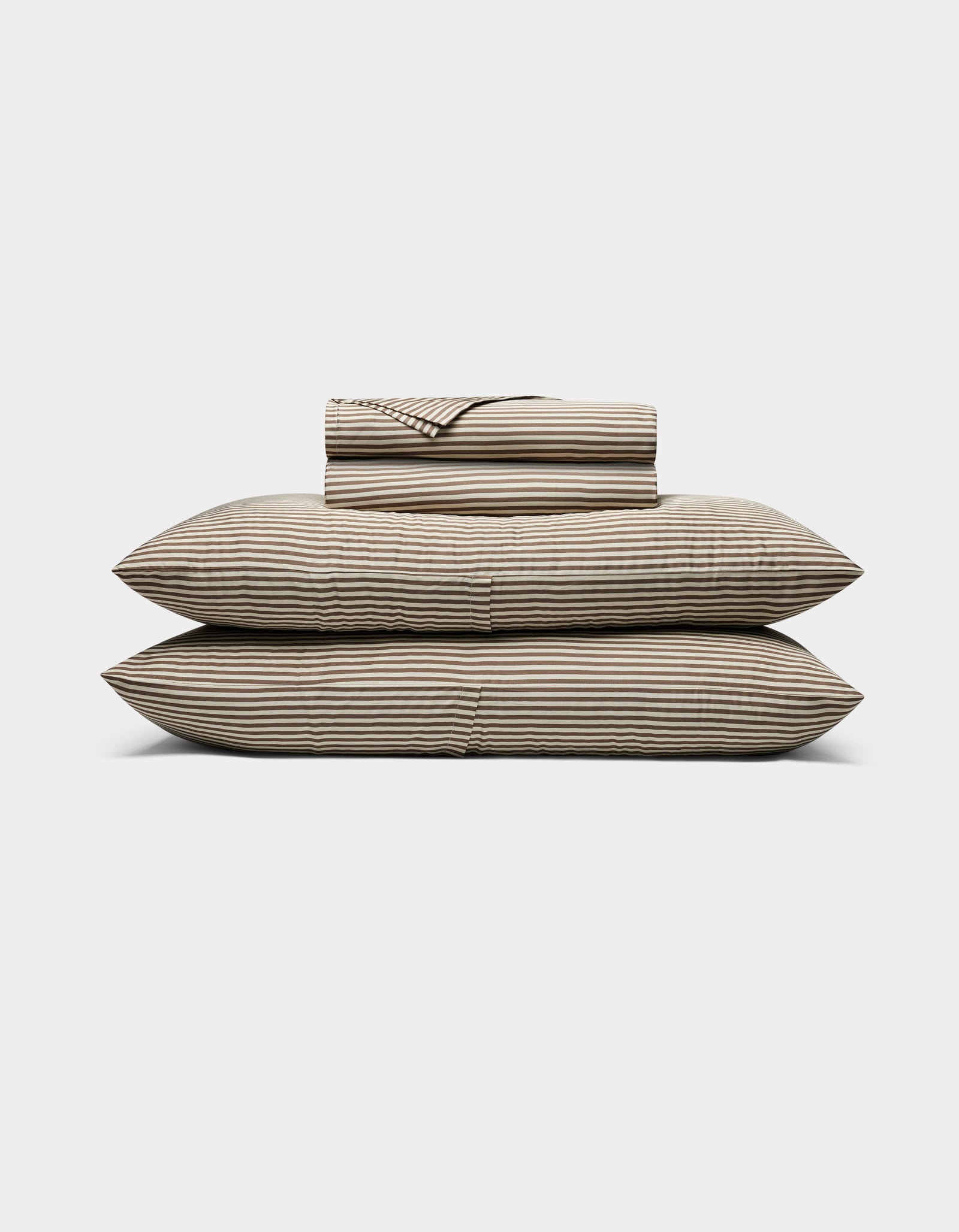 The Cozy Earth Bamboo Sheet Set, featuring striped beige and black sheets and pillowcases, is neatly stacked on two large pillows against a plain white background.