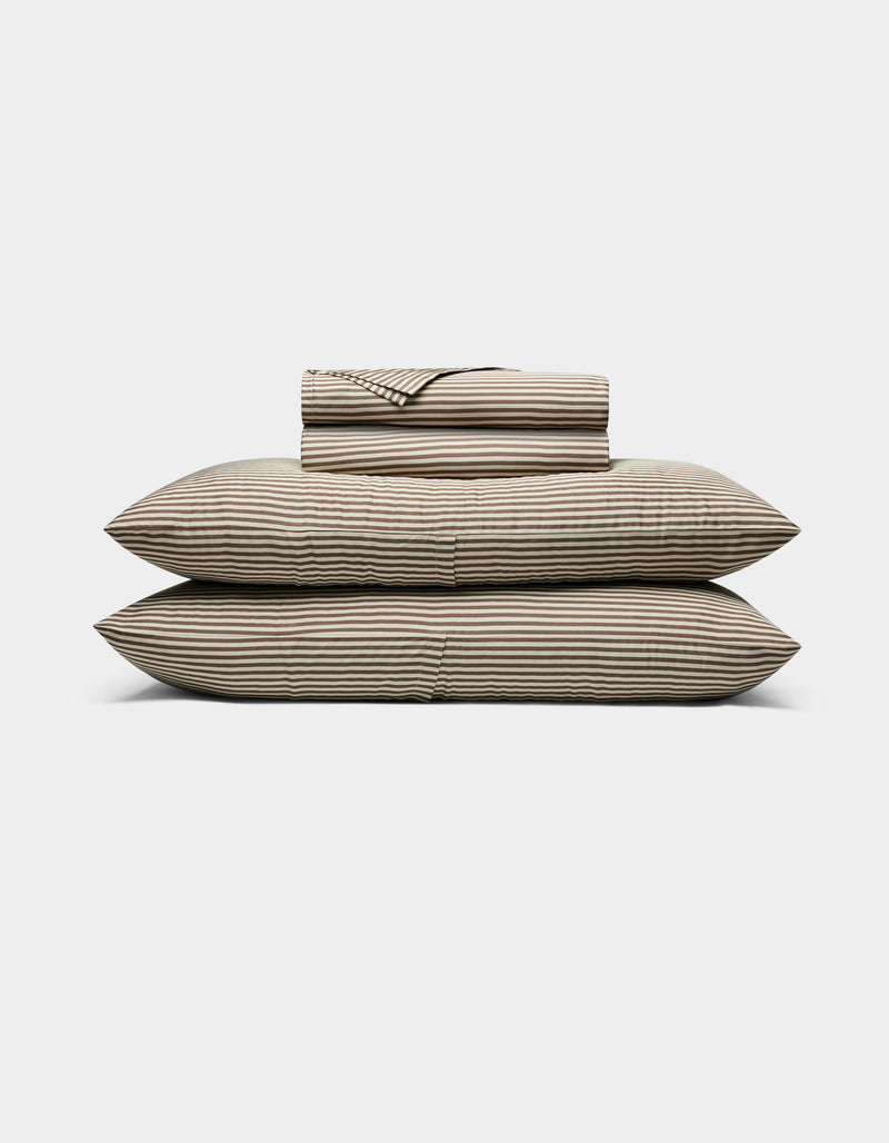 The Cozy Earth Bamboo Sheet Set, featuring striped beige and black sheets and pillowcases, is neatly stacked on two large pillows against a plain white background.