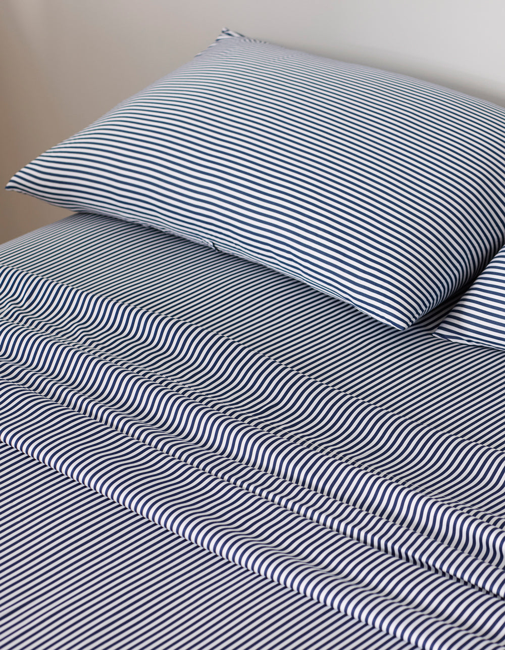 A neatly made bed with Cozy Earth's Bamboo Pillowcases and sheets, featuring thin black-and-white stripes that create an optical illusion effect across the bedding.