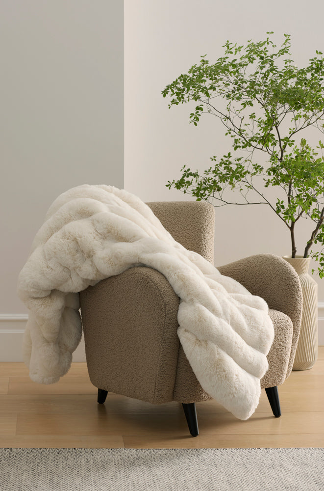 Creme Cozy Earth Channel Cuddle Blanket blanket draped over a beige armchair in a room with a plant.