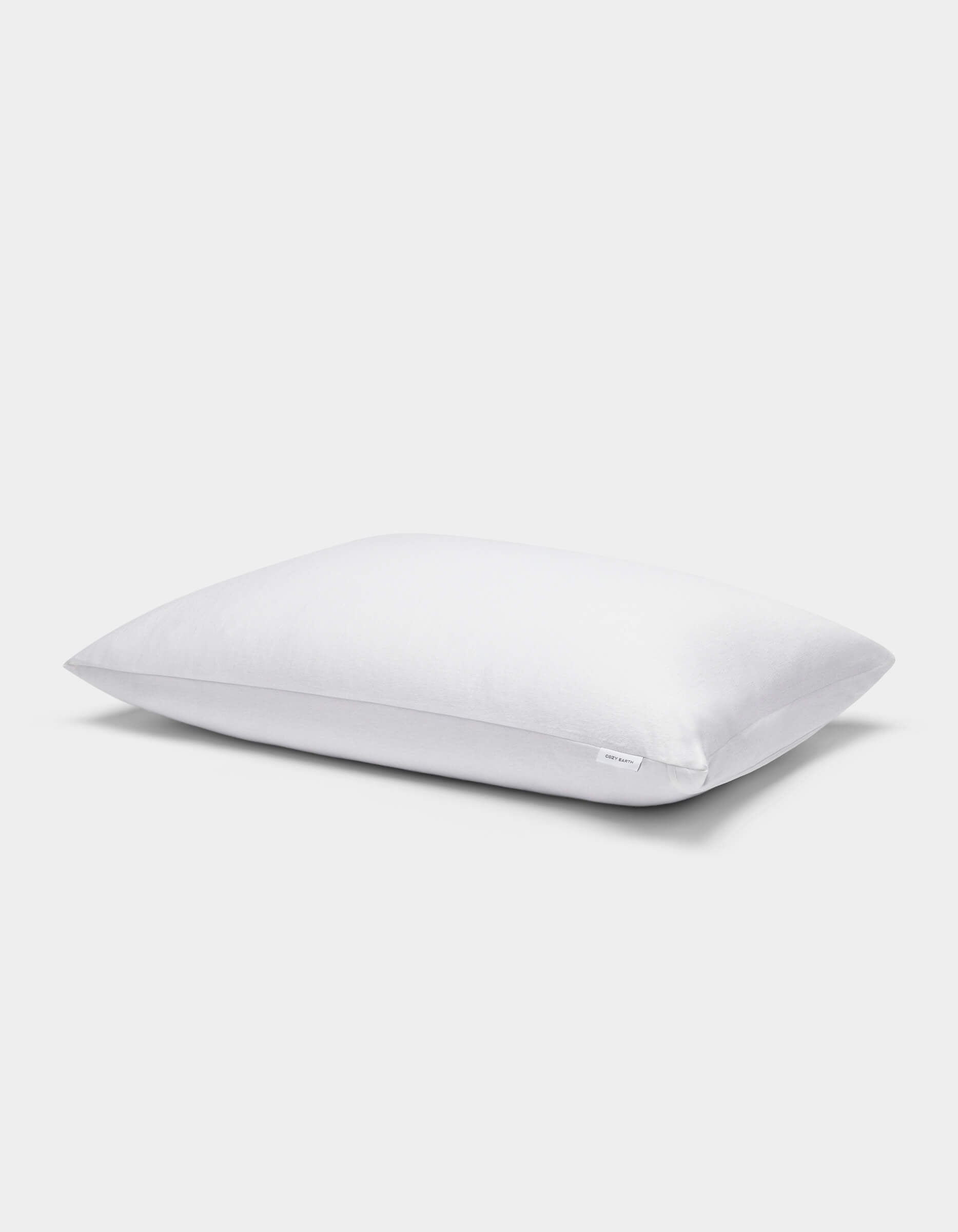 A single Cozy Earth Cooling Pillow Protector in white is displayed against a plain light gray background, featuring a small fabric tag on its side.