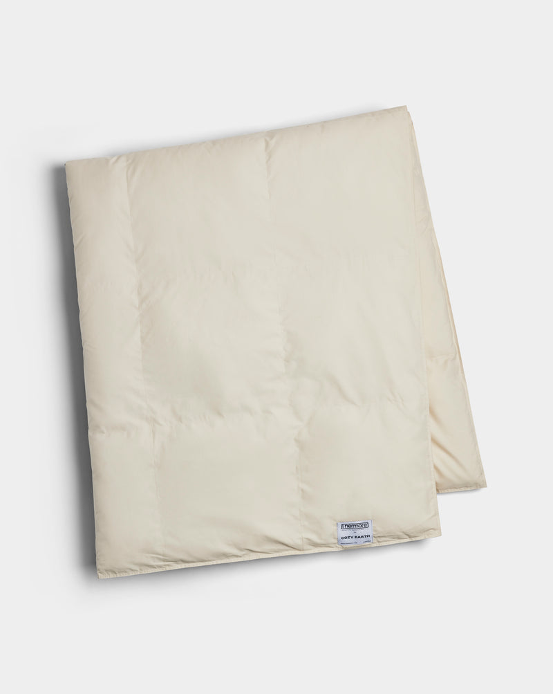 The Cozy Earth Down Alternative Throw is a folded, cream-colored quilt with a small rectangular label near the edge, displayed on a white background.