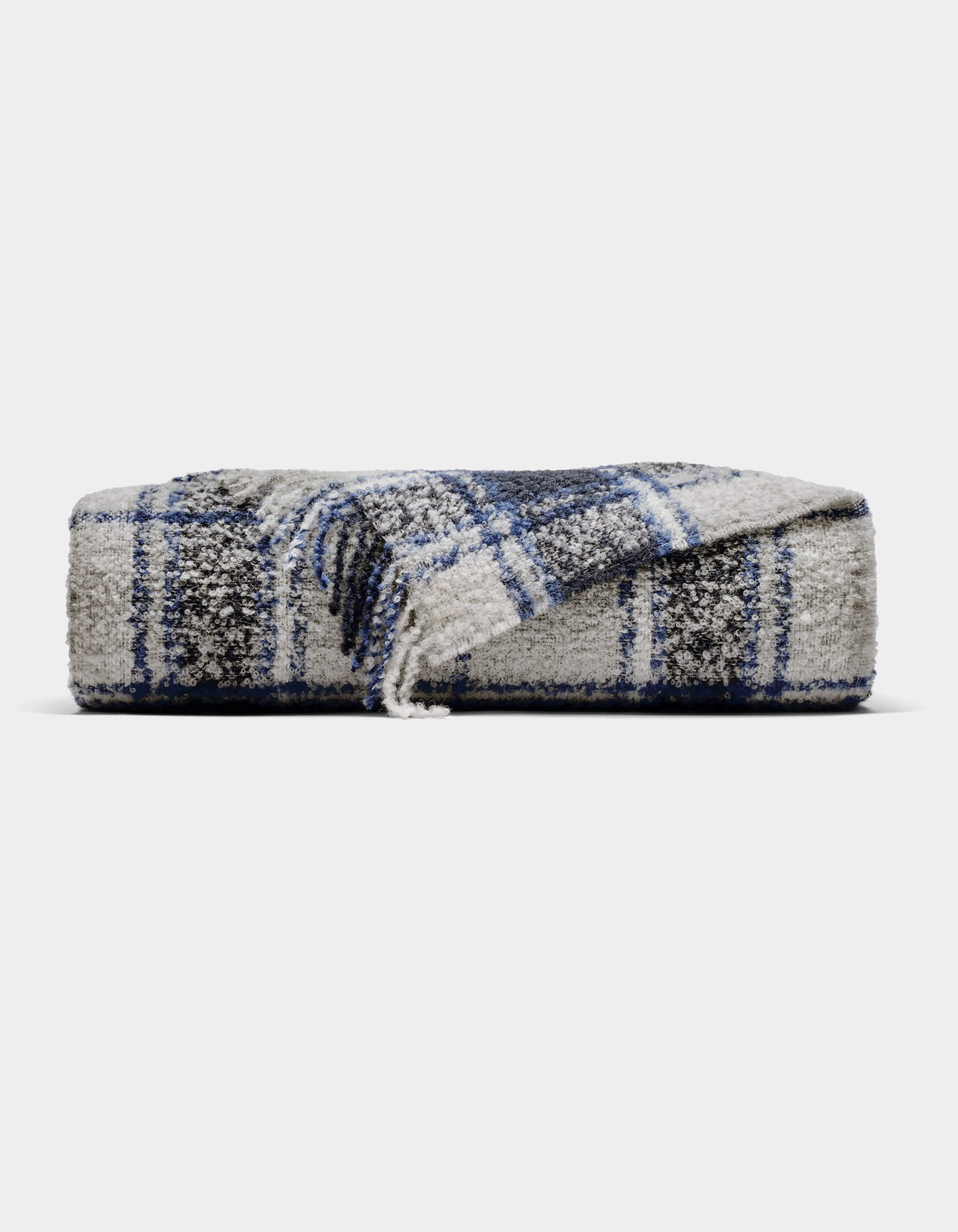 The Cozy Earth Alpaca Boucle Throw is a soft, gray blanket with a blue and white plaid pattern. Displayed against a plain background, one corner is partially unfolded to showcase its unique texture and design.|Color:Indigo Plaid