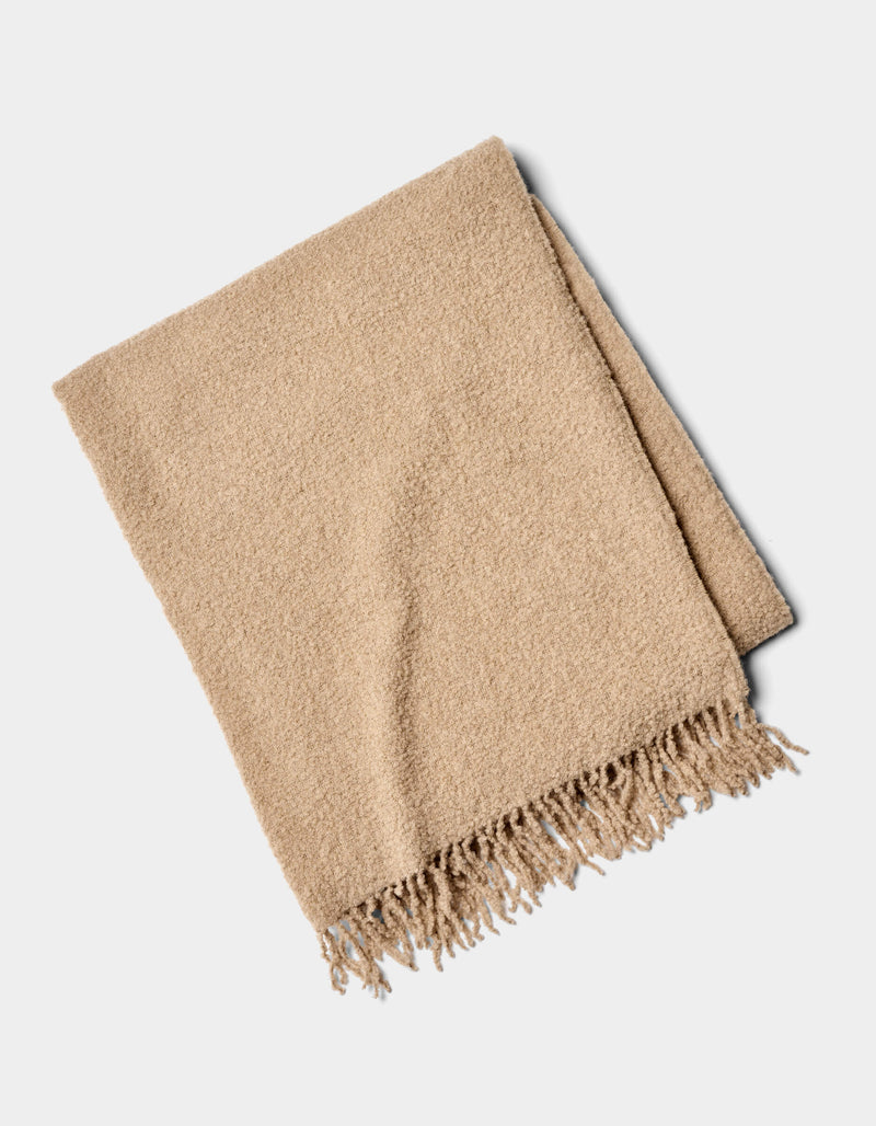 The Alpaca Boucle Throw by Cozy Earth is a beige blanket with a soft, textured surface and fringed edges, shown folded on a plain white background.