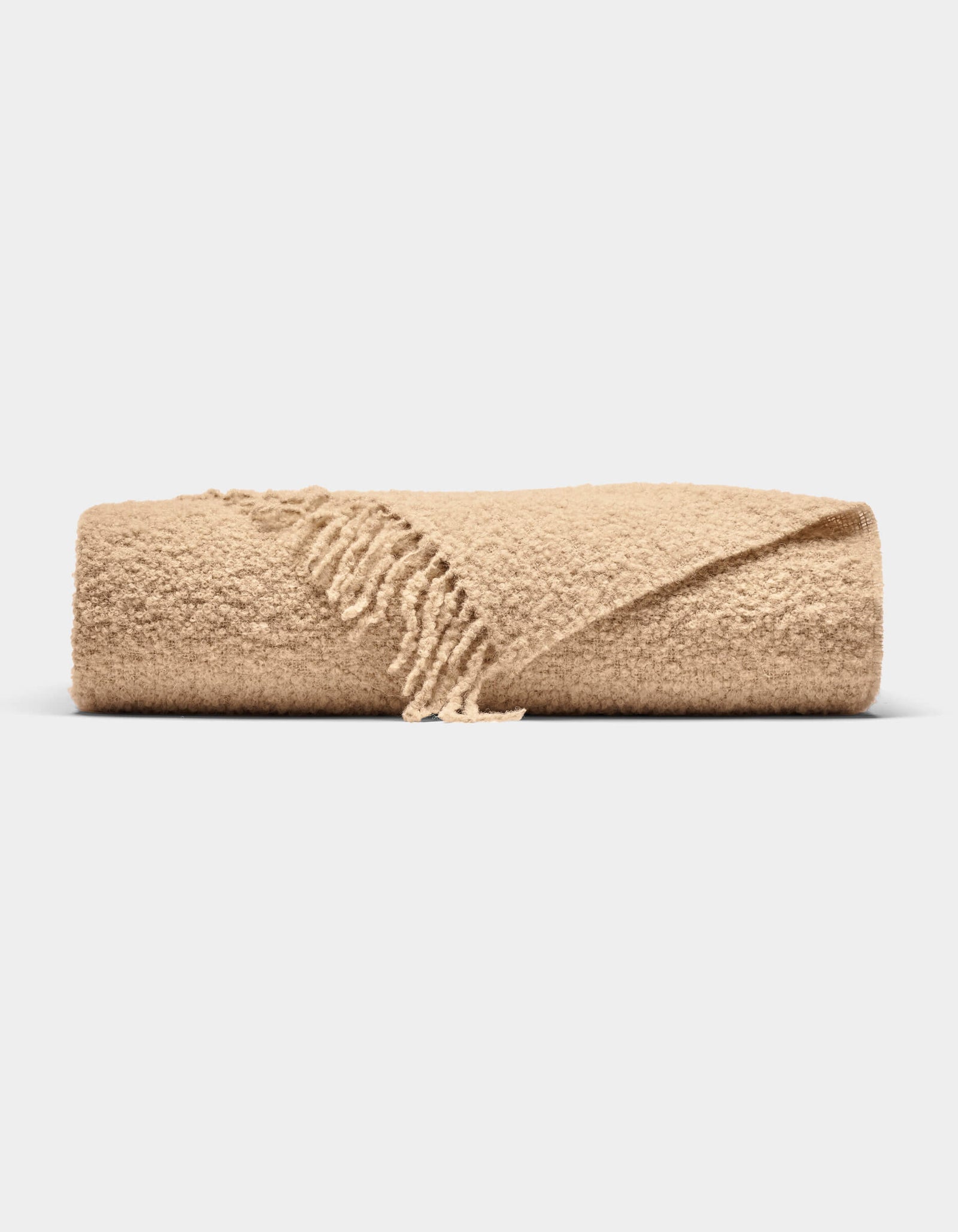 The Cozy Earth Alpaca Boucle Throw, featuring a textured surface and fringed edges in beige, is neatly folded and displayed against a plain white background.