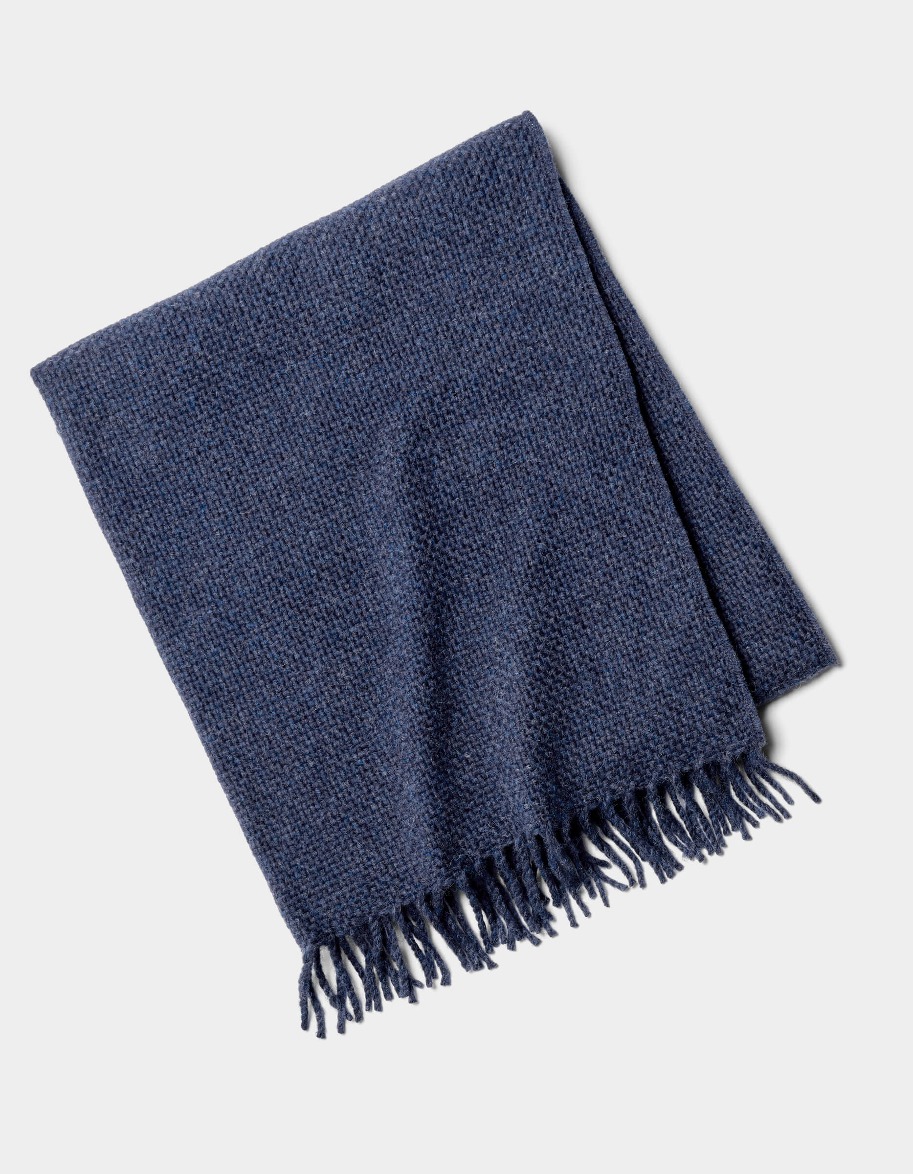 The Cozy Earth Lucia Throw, a folded dark blue woven blanket with fringe tassels on one edge, is displayed against a light gray background.