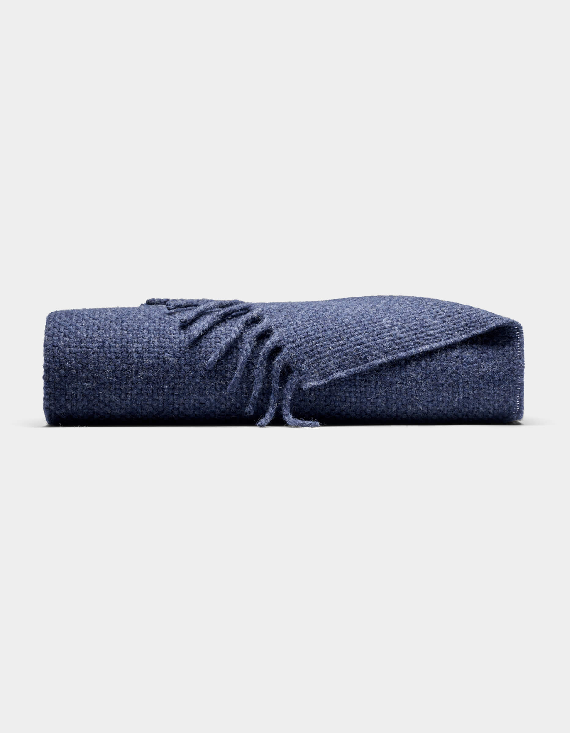 The Cozy Earth Lucia Throw, featuring a textured blue design and fringed edges, is neatly folded and displayed against a plain light gray background.