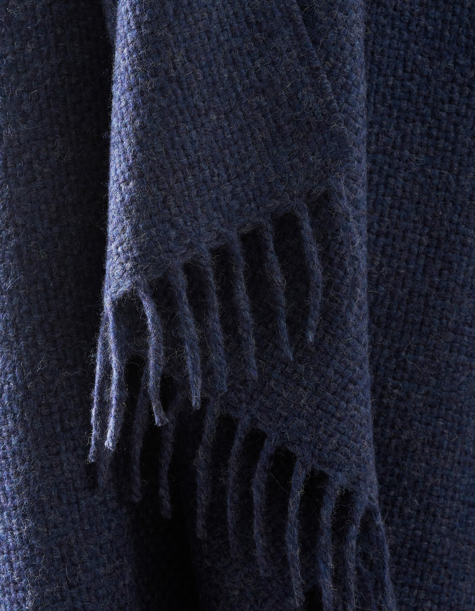 A close-up of the Lucia Throw by Cozy Earth shows its dark blue, textured woven fabric with fringed edges hanging down.|Color:Indigo