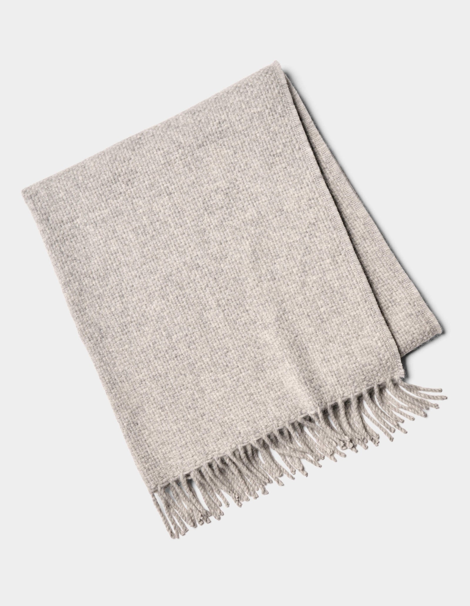 The Lucia Throw by Cozy Earth is a folded light gray woven blanket with fringe on one side, shown on a white background.
