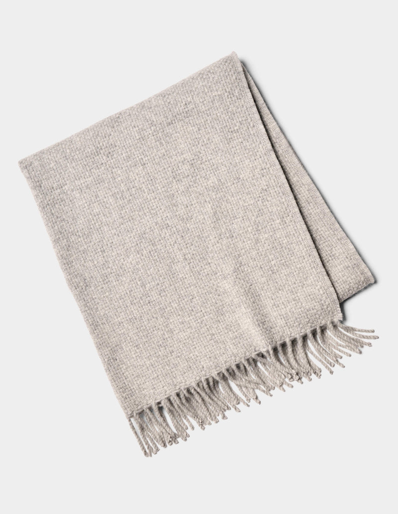 The Lucia Throw by Cozy Earth is a folded light gray woven blanket with fringe on one side, shown on a white background.