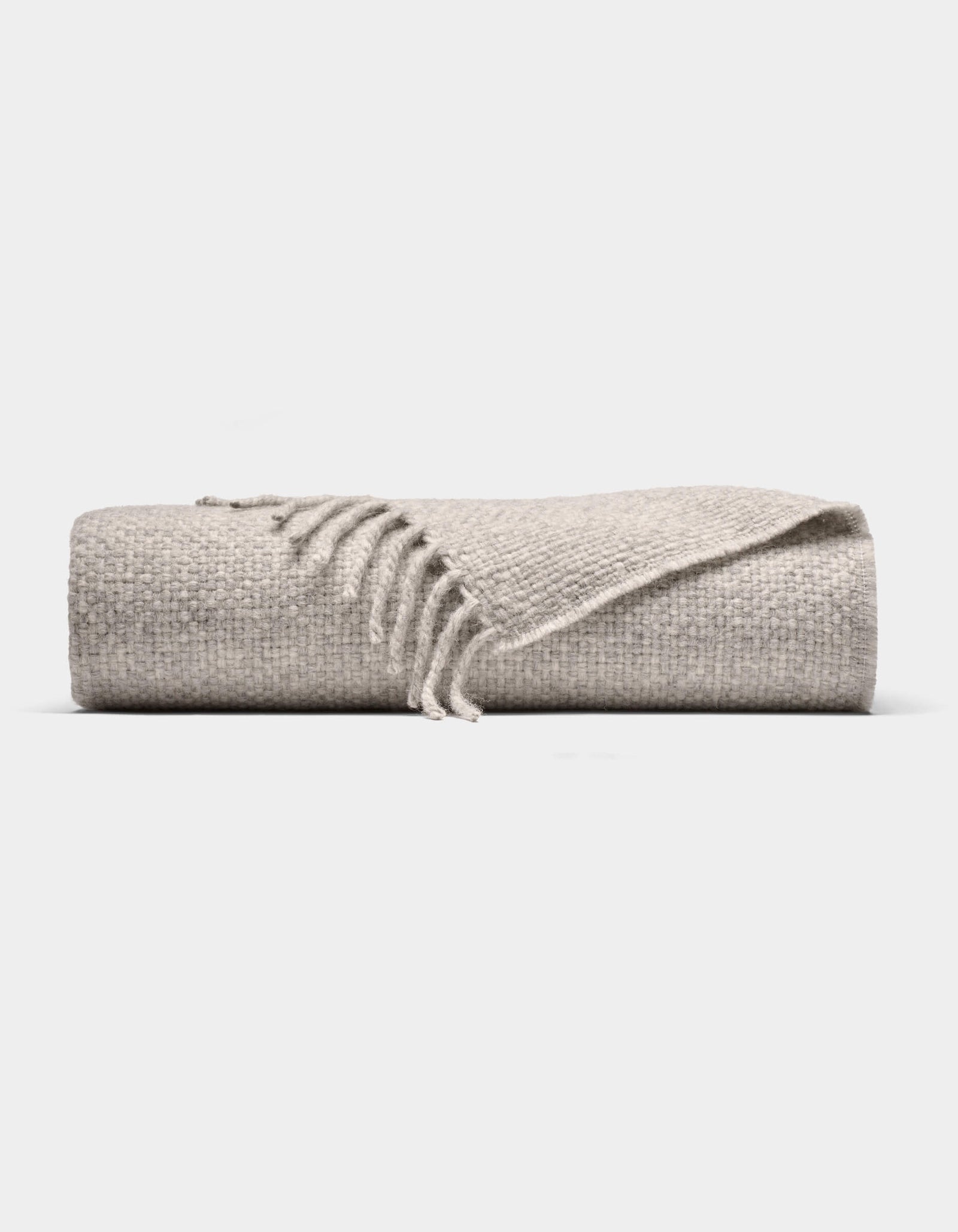 The Cozy Earth Lucia Throw is a folded light gray woven blanket with a textured surface and fringe on one end, shown against a plain white background.