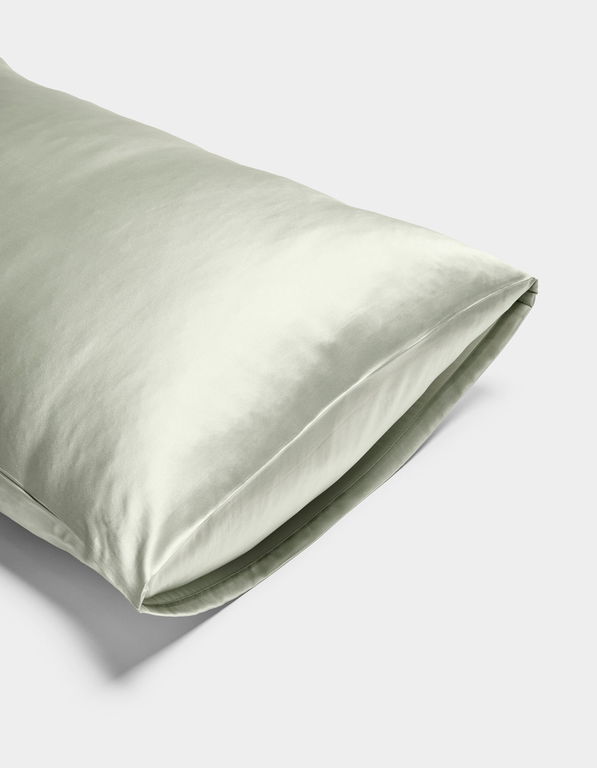 A close-up of the Cozy Earth Silk Pillowcase in light green, featuring a smooth, shiny texture, displayed on a plain white background.