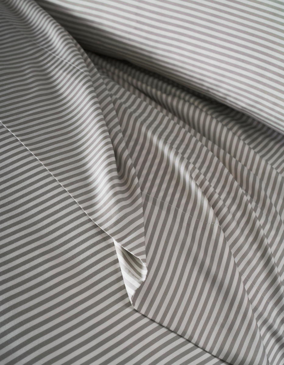 Close-up of Cozy Earth's Bamboo Duvet Cover, neatly arranged with thin gray and white horizontal stripes. The top layer is slightly folded, showcasing the matching striped pattern.