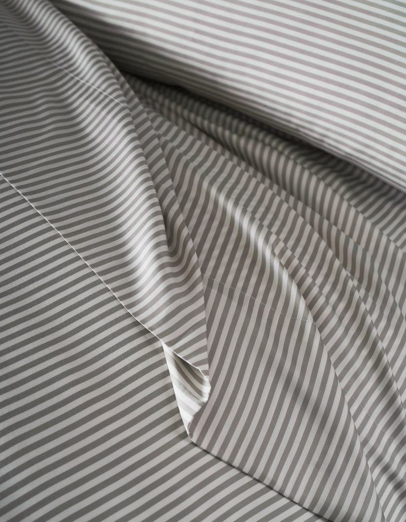 Close-up of Cozy Earth's Bamboo Duvet Cover, neatly arranged with thin gray and white horizontal stripes. The top layer is slightly folded, showcasing the matching striped pattern.