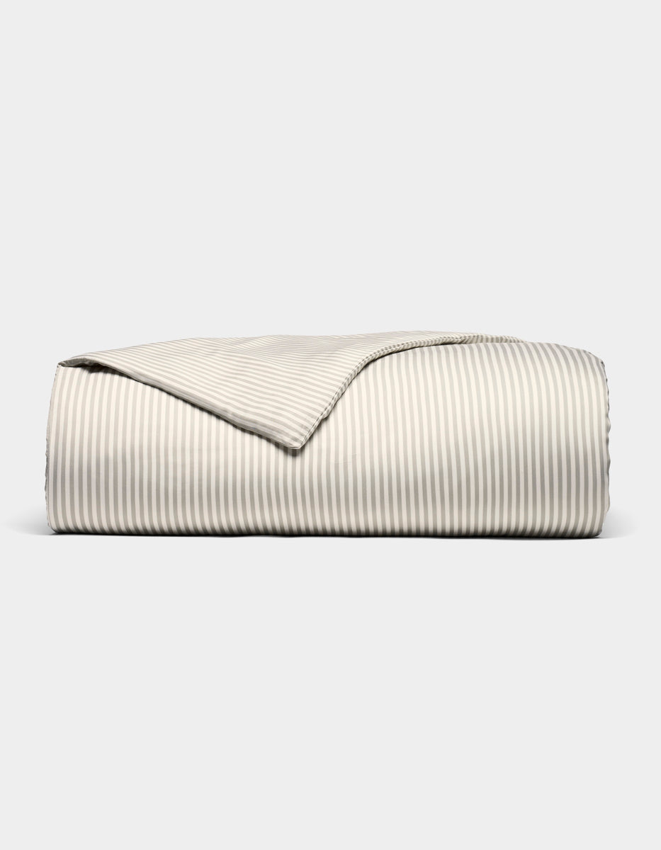 Cozy Earth's Bamboo Duvet Cover is displayed neatly folded on a light gray background, with one corner turned back to showcase its beige and white striped design inside and out.|Color:Classic Stripe in Laurel