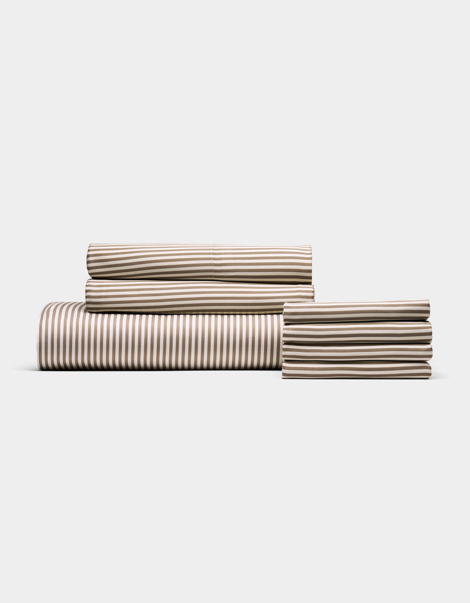 The Cozy Earth Bamboo Bedding Core Bundle features a neatly folded set of tan and white striped sheets—including a fitted sheet, flat sheet, and pillowcases—displayed against a plain white background.
