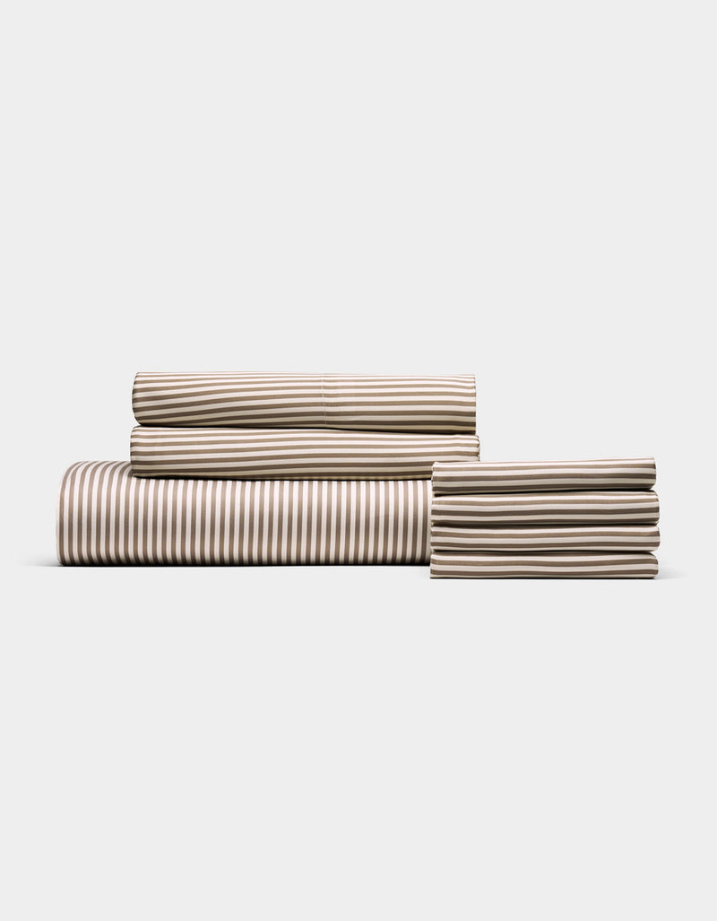 The Cozy Earth Bamboo Bedding Core Bundle features a neatly folded set of tan and white striped sheets—including a fitted sheet, flat sheet, and pillowcases—displayed against a plain white background.