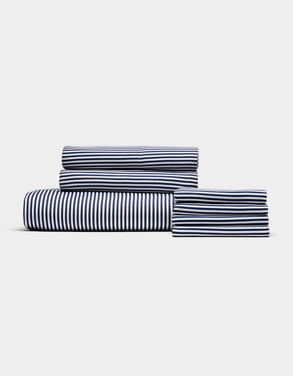 The Bamboo Bedding Core Bundle by Cozy Earth, featuring neatly folded navy and white striped sheets and pillowcases, is stacked against a plain light gray background.
