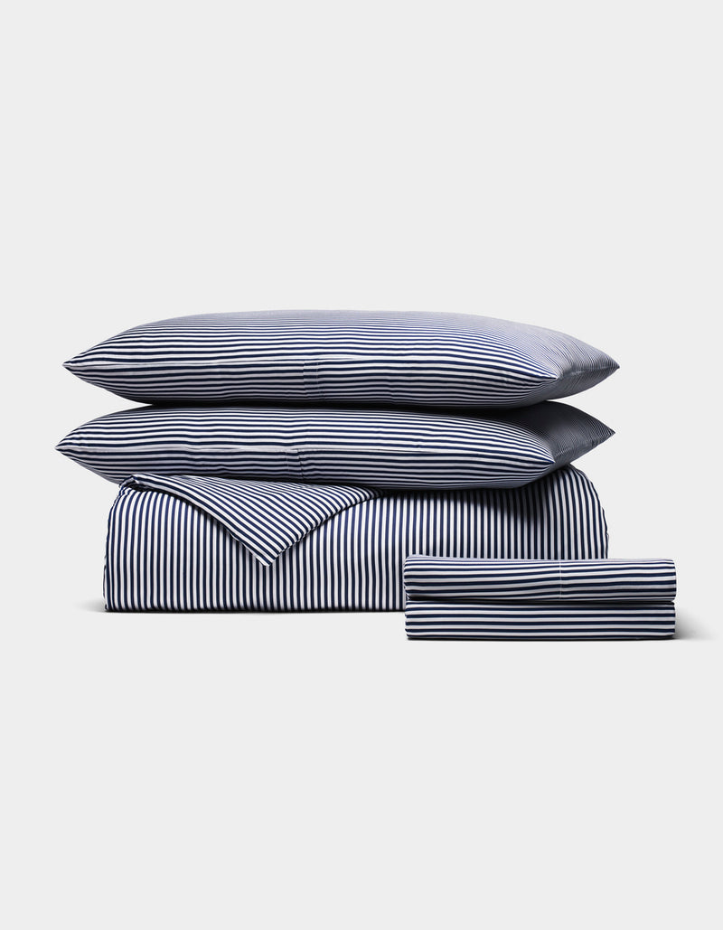 The Cozy Earth Bamboo Bedding Deluxe Bundle, featuring two pillows, a duvet, and sheets with navy and white vertical stripes, is neatly folded and displayed against a plain light background.