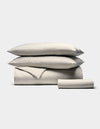 The Bamboo Bedding Essential Bundle by Cozy Earth features a neatly stacked set of beige and white striped bedding—two pillows, a folded duvet, and a folded sheet—displayed on a plain light background.|Color:Classic Stripe in Laurel