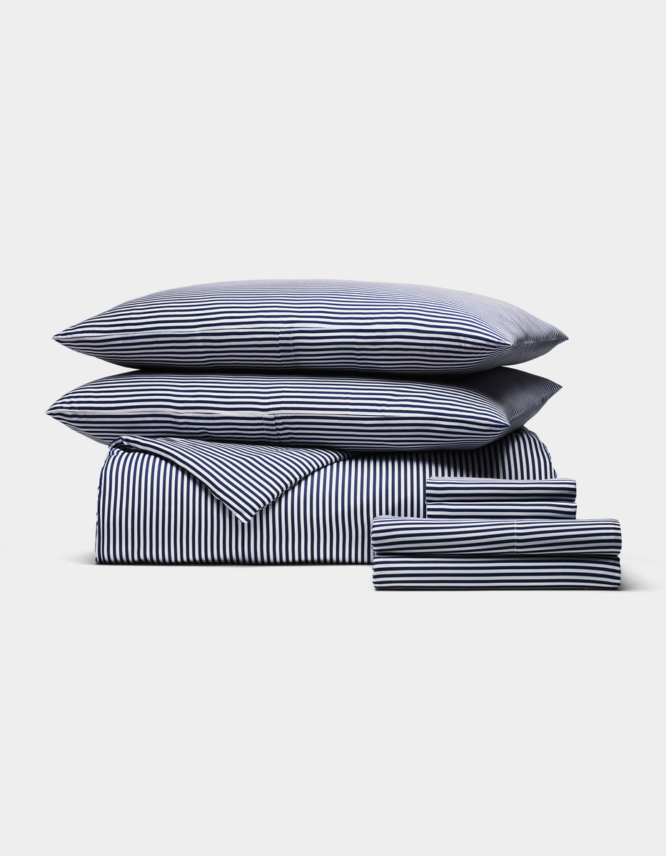 The Cozy Earth Bamboo Bedding Ultimate Bundle, featuring navy blue and white stripes, includes a duvet, sheet, two pillows, and two pillowcases, all neatly arranged on a plain white background.