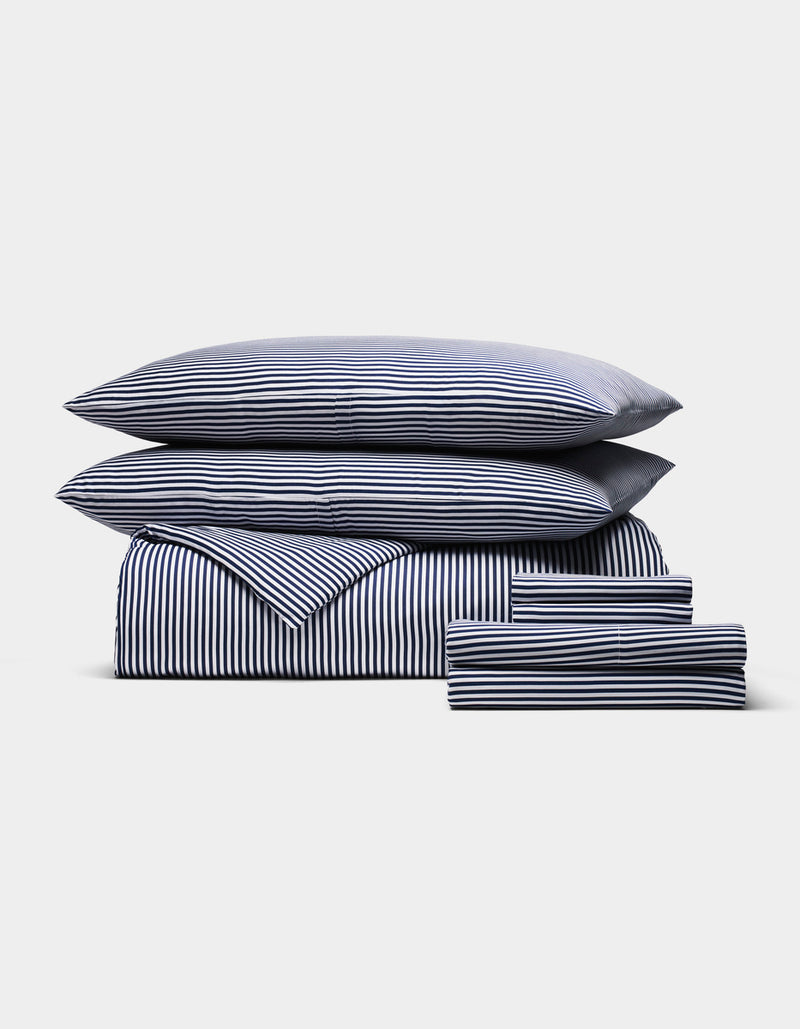 The Cozy Earth Bamboo Bedding Ultimate Bundle, featuring navy blue and white stripes, includes a duvet, sheet, two pillows, and two pillowcases, all neatly arranged on a plain white background.