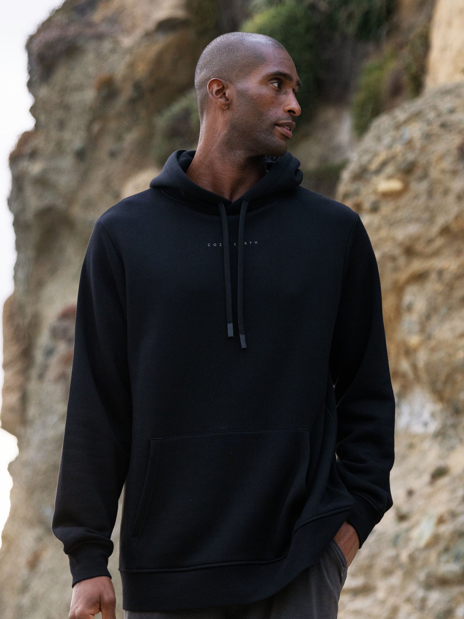 Man wearing black cityscape hoodie with rocky backdrop 