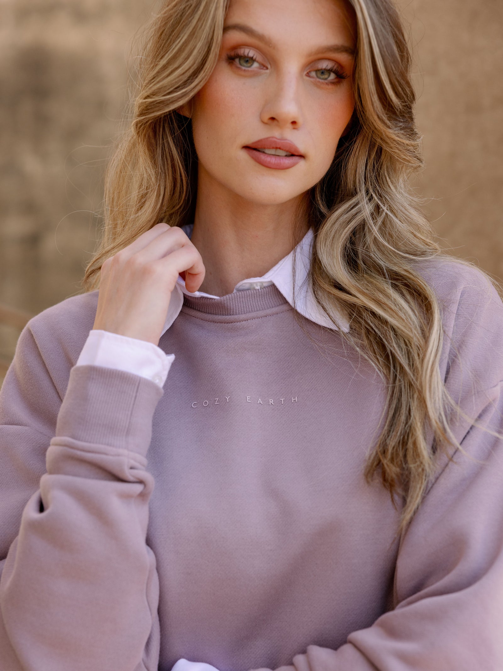 Dusty Orchid CityScape Pullover Crew. The Pullover is being worn by a female model. Accompanying city scape clothing is being worn to complete the look of the outfit. The photo was taken with a city building in the background. 