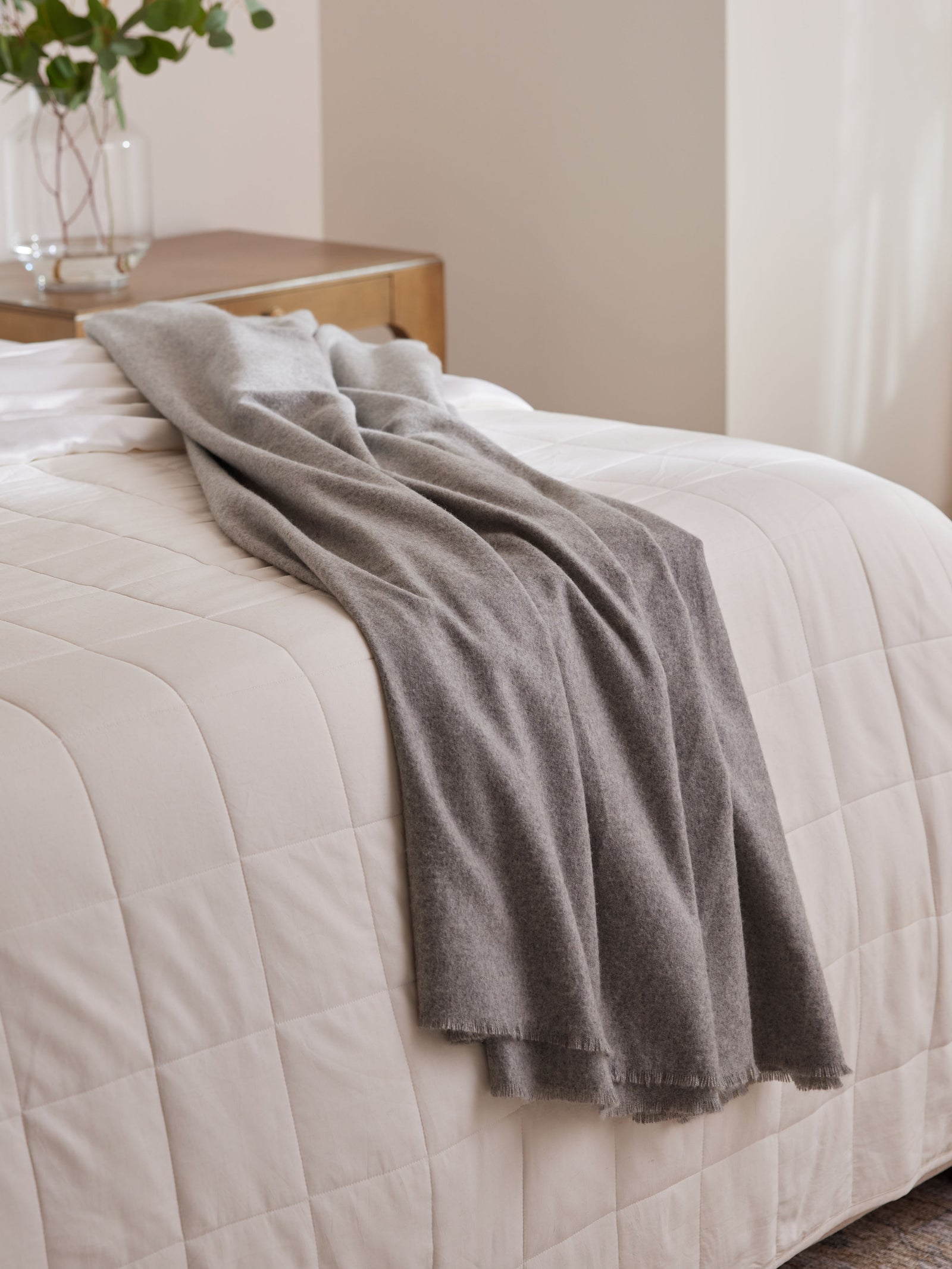 Pebble Fringe blanket draped on bed with white comforter 