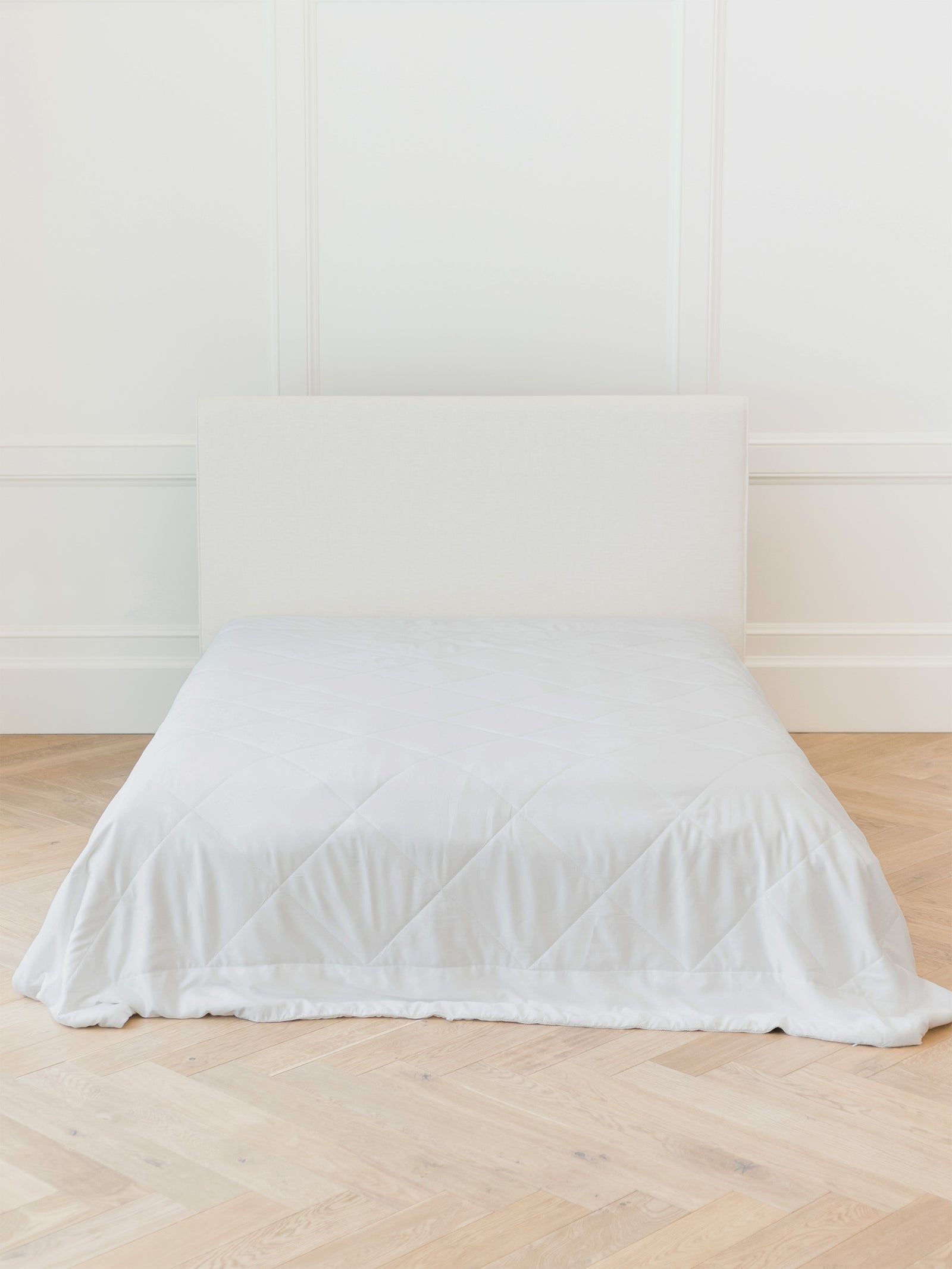 A neatly made bed with a white headboard and the Cozy Earth Bamboo Viscose Comforter, set on light wood herringbone flooring against a white paneled wall. 