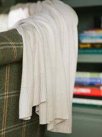 Beige Mini-Knit Blanket. The blanket is hanging from a green couch. The edge of the blanket is photographed up close so as to show the texture of the edge of the blanket.|Color:Beige