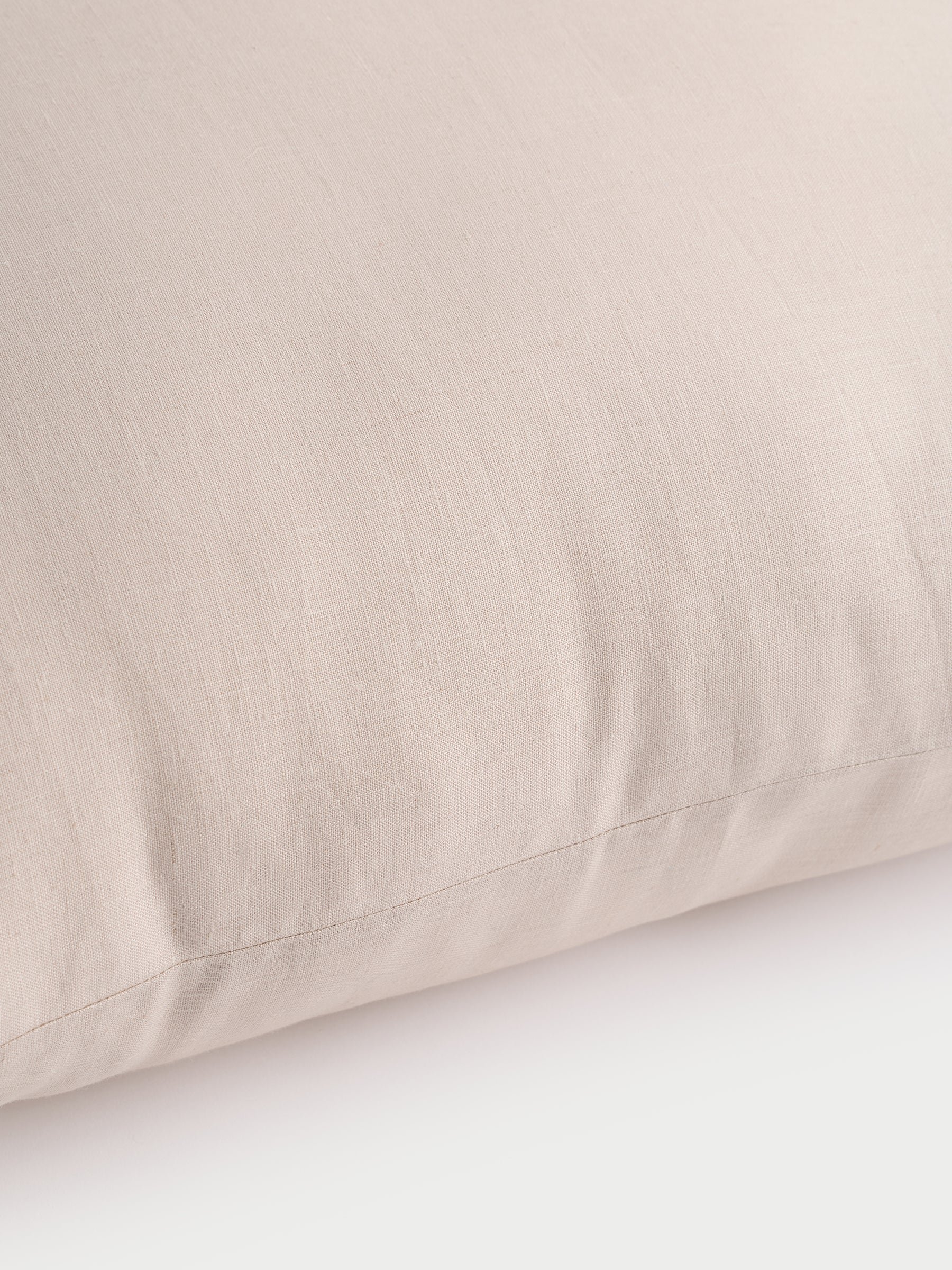 Close-up image of a Linen Throw Pillow by Cozy Earth, featuring a beige hue with a smooth, slightly crinkled fabric surface, resting on a white background. The pillow boasts a minimalist and neutral appearance that highlights its texture and subtle stitching. |Color:Birch|Size:14" x 30"