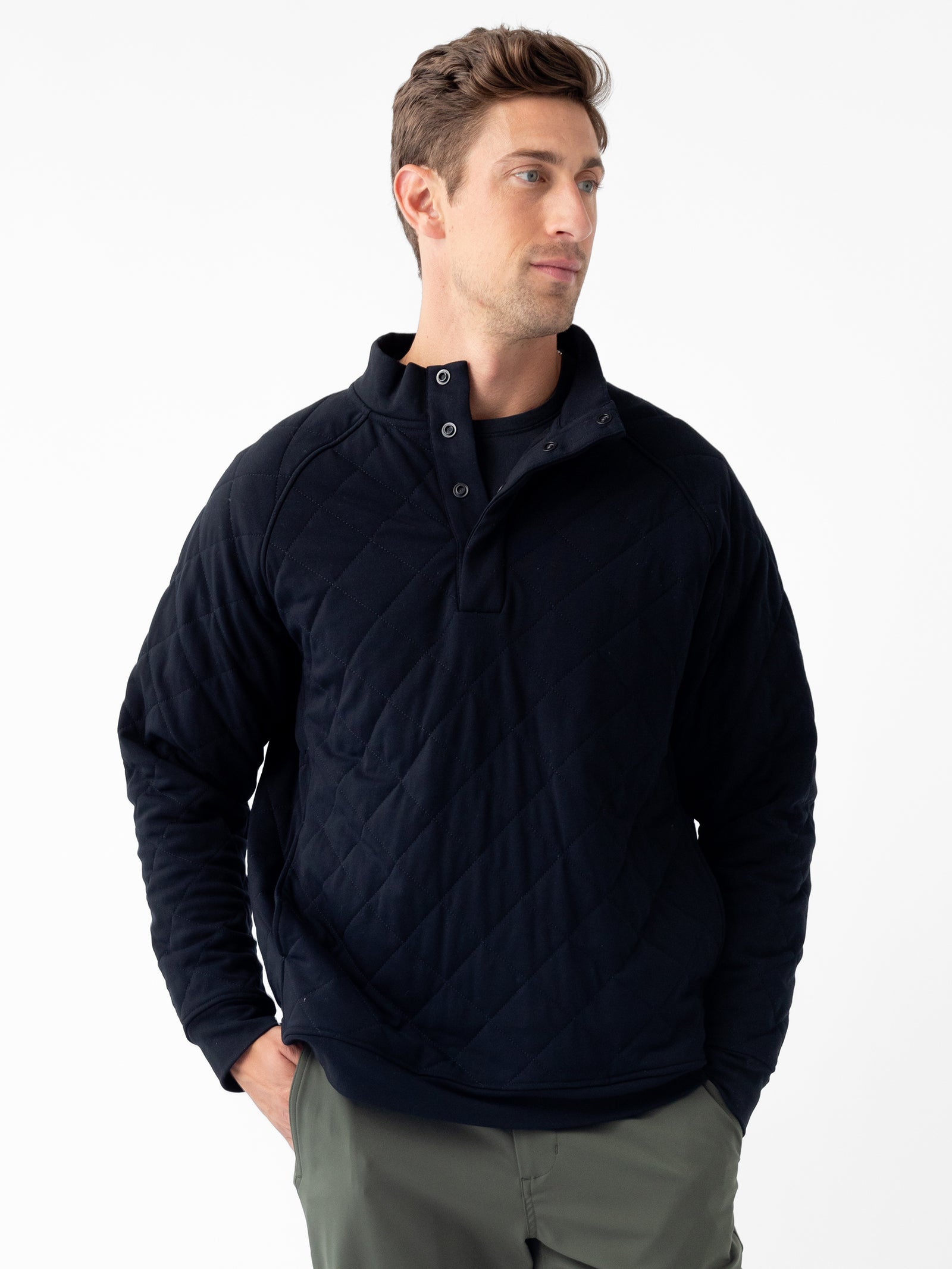 A person stands against a white background wearing Cozy Earth's Men's Ultra-Soft Bamboo Quilted Snap Pullover, which features a high collar and button placket. Their hands are tucked into the pockets of their gray pants, and they are looking slightly to the left with a neutral expression. 