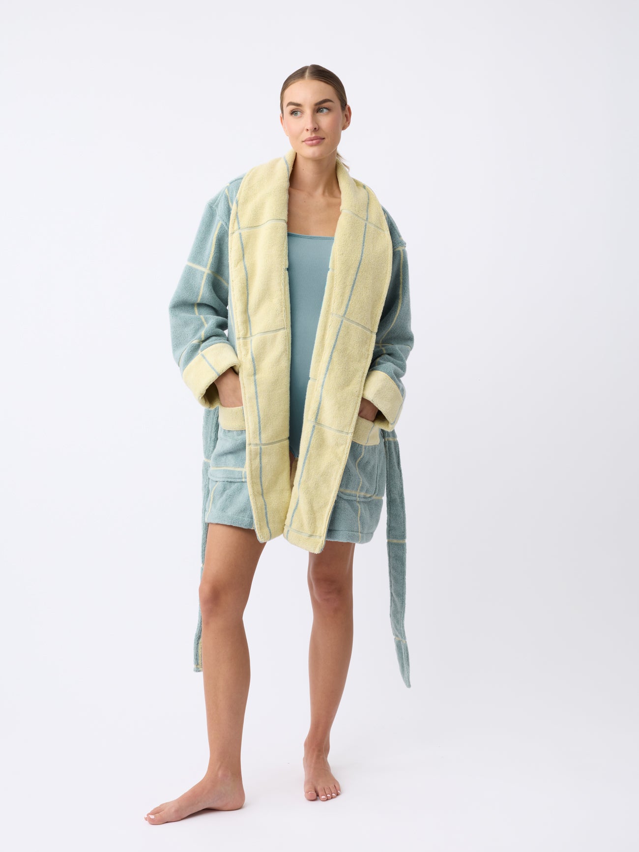 A person models the Cozy Earth Windowpane Resort Robe in teal and yellow checkered fabric over a light blue outfit. They stand barefoot with one hand in a pocket against a plain white background. |Color:Blue Lagoon