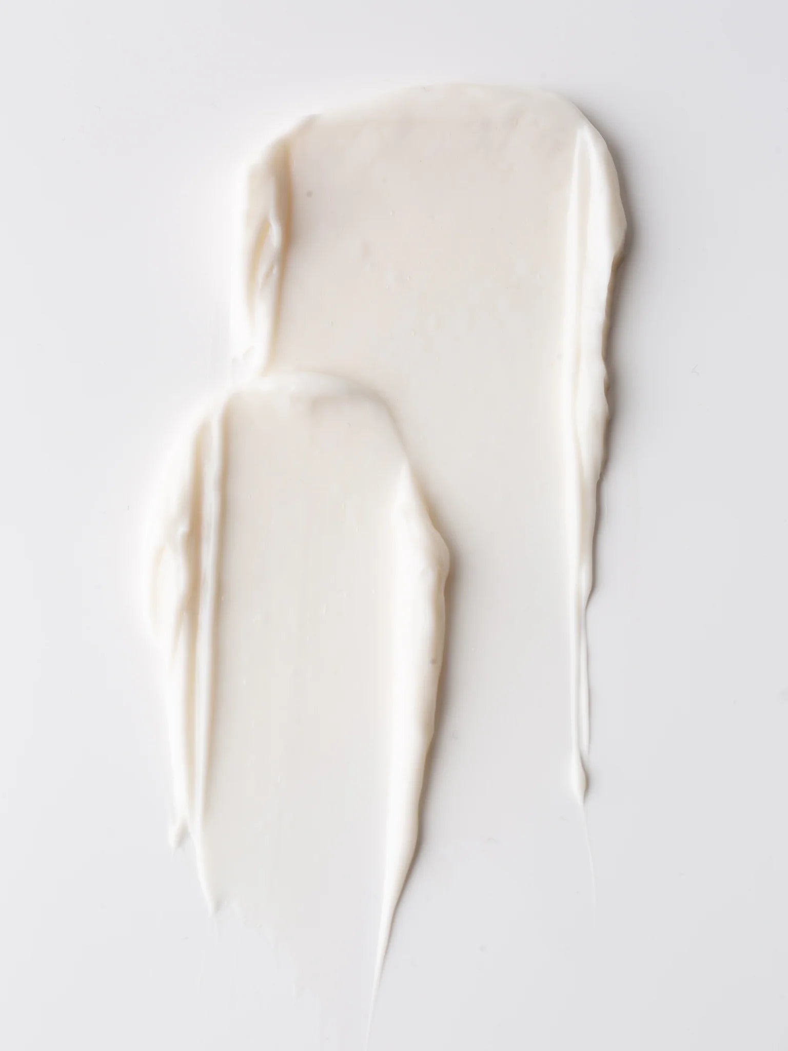 Streaks of a creamy, white substance on a plain white background resemble Cozy Earth's Bedtime Bundle moisturizer with a smooth and slightly glossy texture.