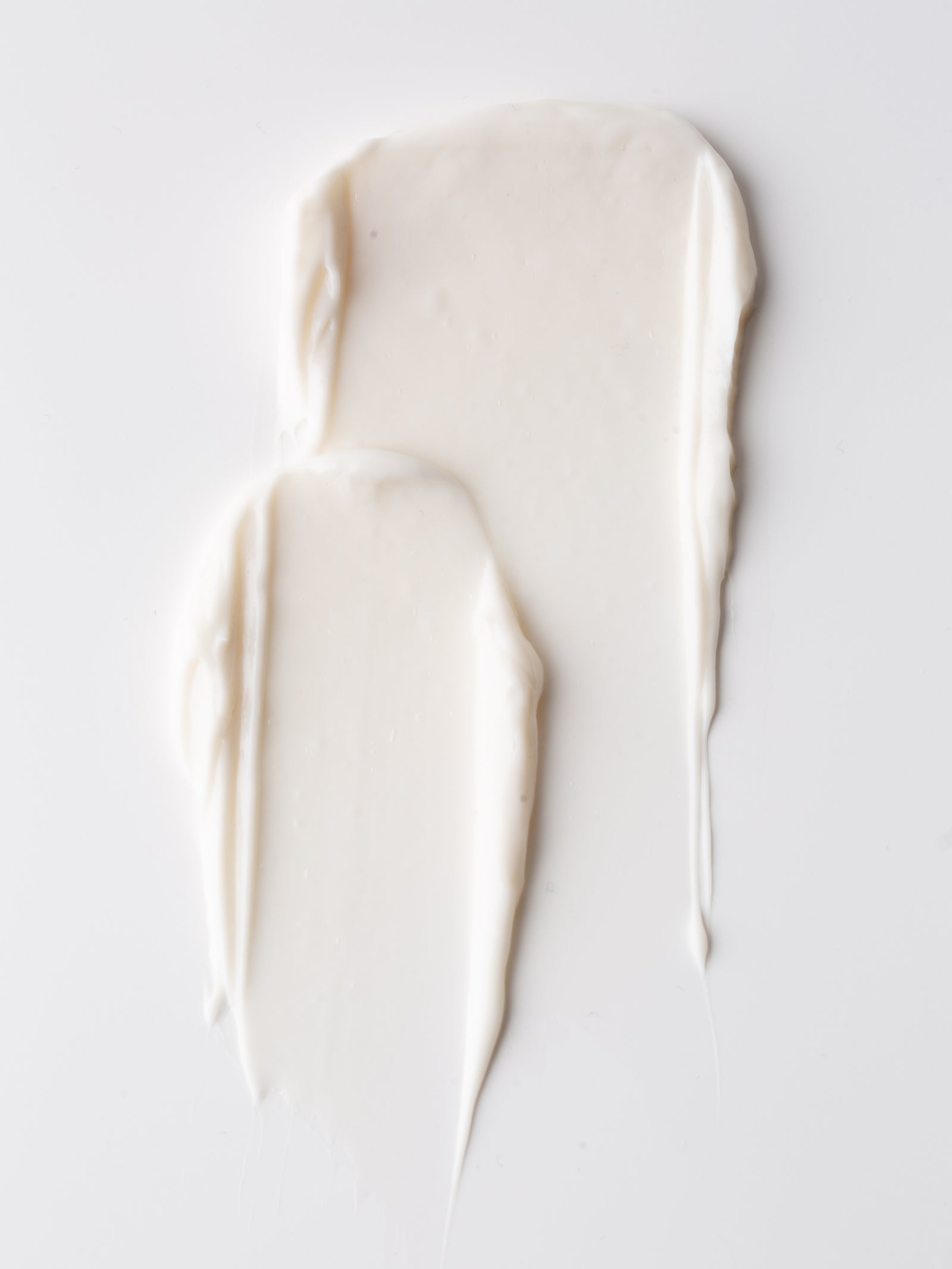 Two smears of Cozy Earth Body Butter, creamy white in color, rest on a smooth white surface for a minimalistic and clean look.