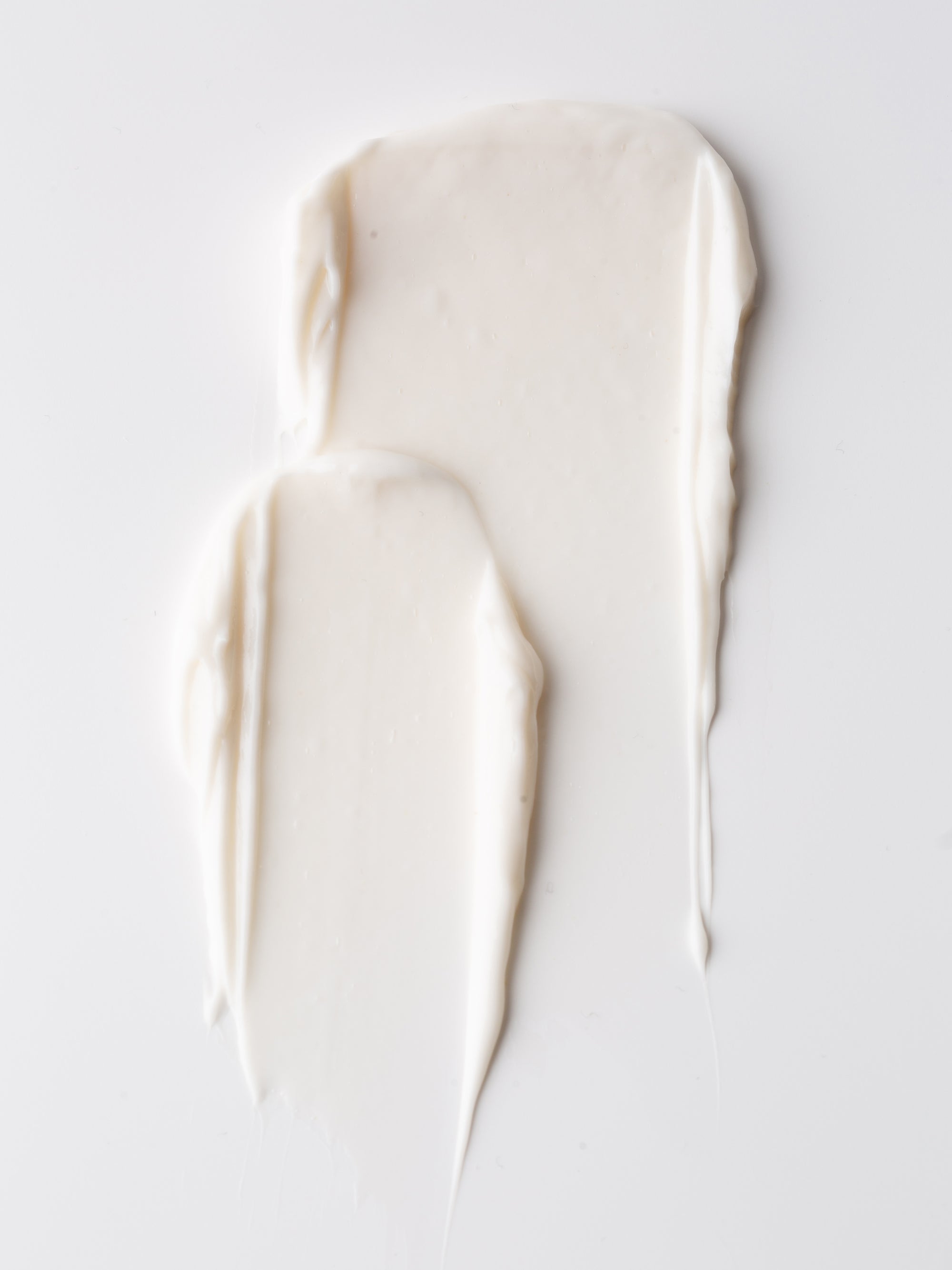 Two smears of Cozy Earth Body Butter, creamy white in color, rest on a smooth white surface for a minimalistic and clean look.