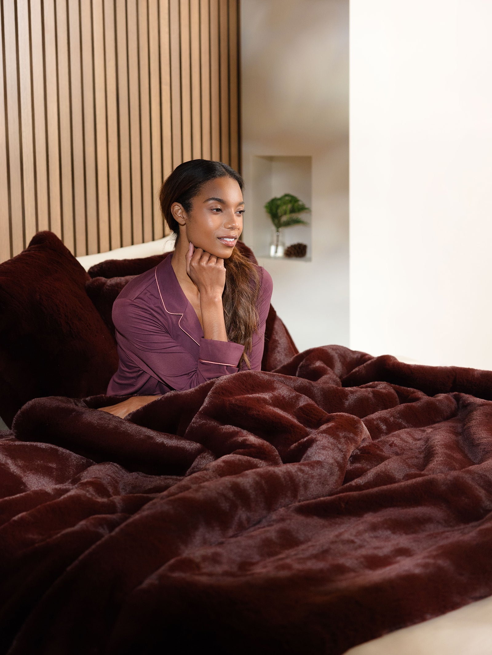 Woman sitting on bed with burgundy oversized throw cuddle blanket 