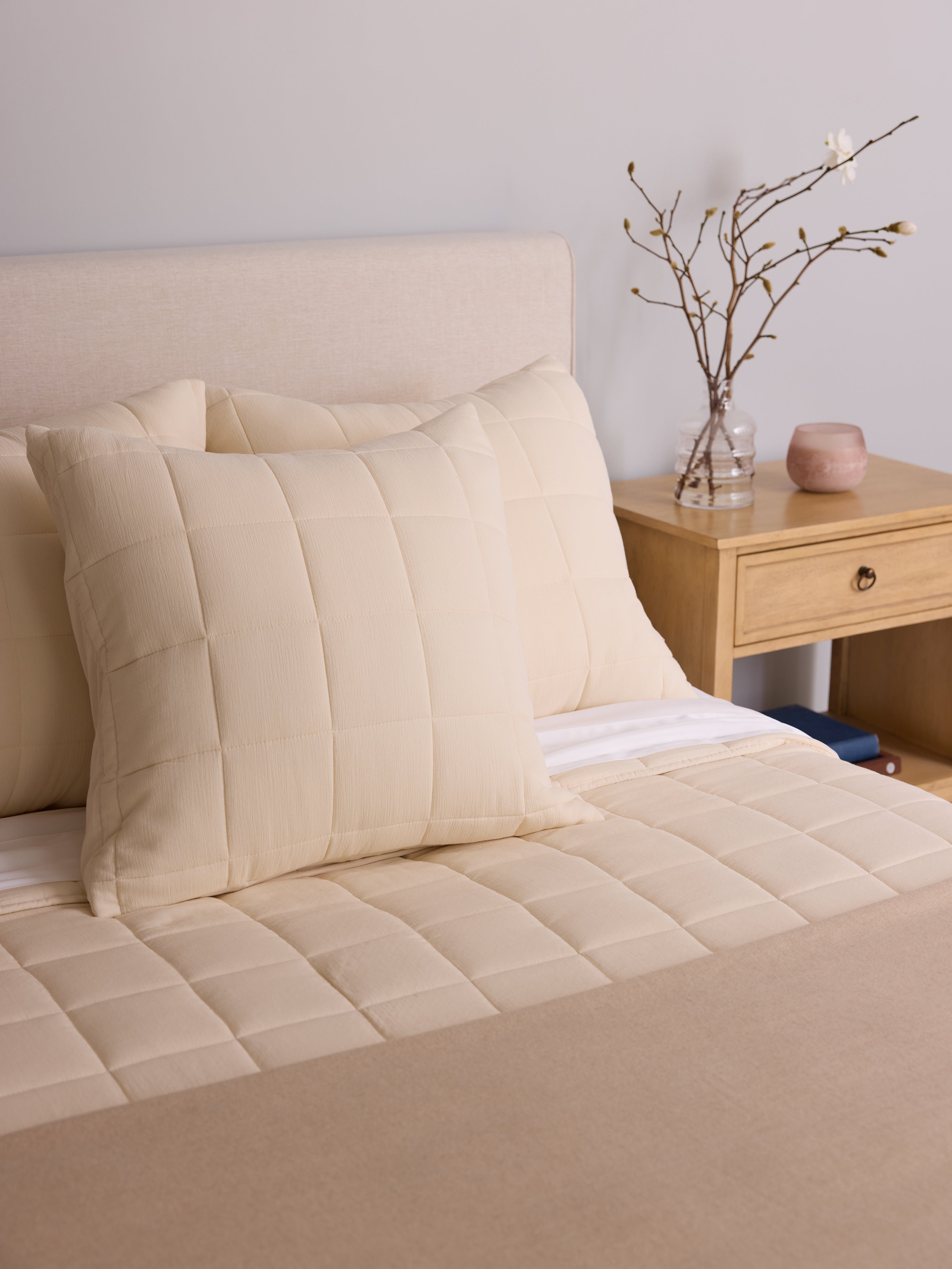 Buttermilk Aire Bamboo Box Quilt Euro Sham. The sham is resting on a bed in a bedroom|Color:Buttermilk|Size:Euro