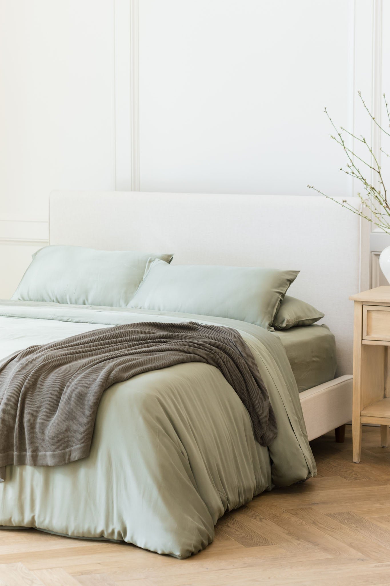 Charcoal cloud knit blanket draped over bed with sage bedding 