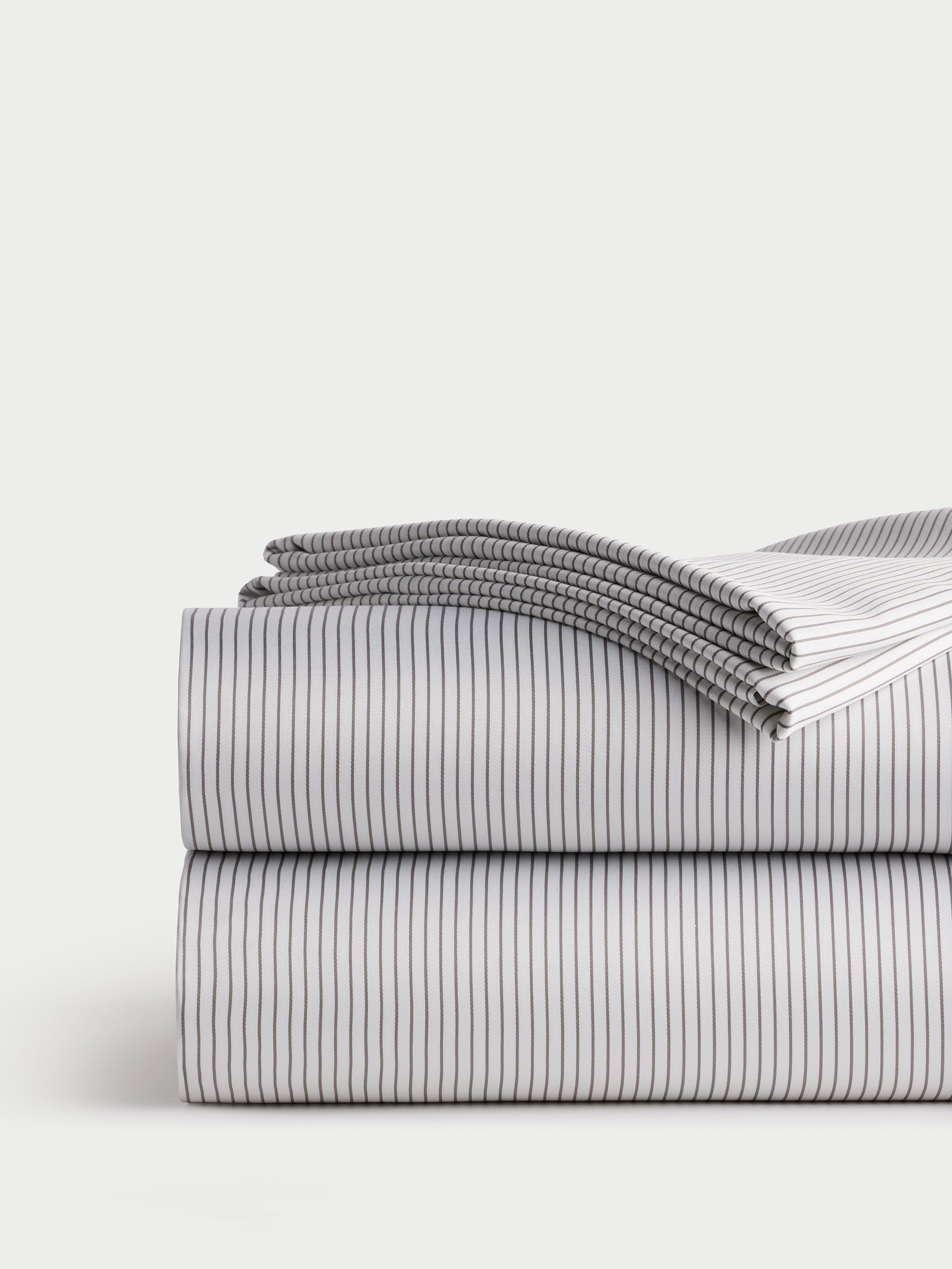 A neatly folded stack of Cozy Earth's Bamboo Sheet Set, featuring a clean white design with thin black stripes set against a neutral background. The top sheet is partially unfolded, displaying the elegant striped pattern. 