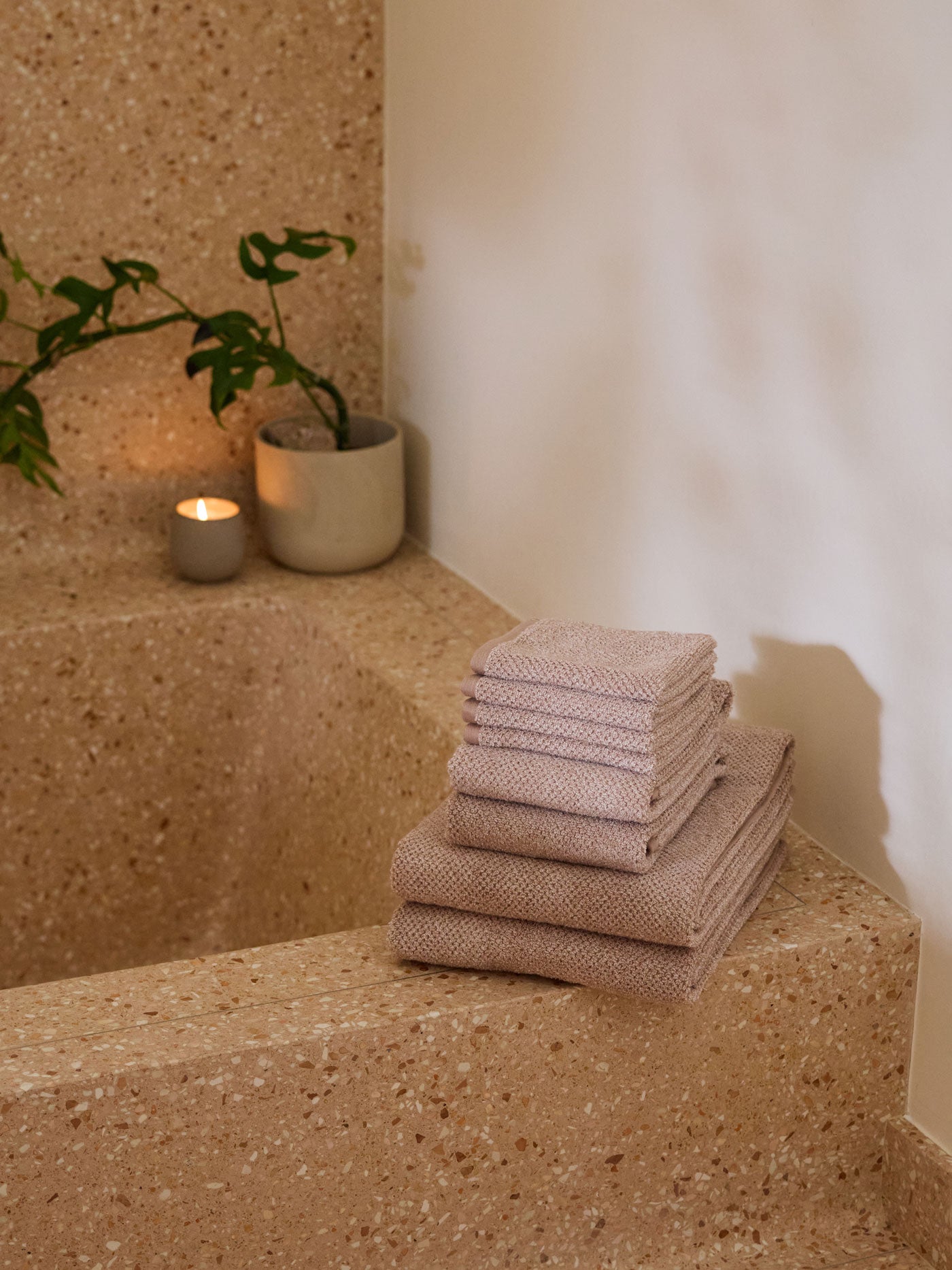 A stack of Cozy Earth bath towels sit on the edge of a stone bathtub. 