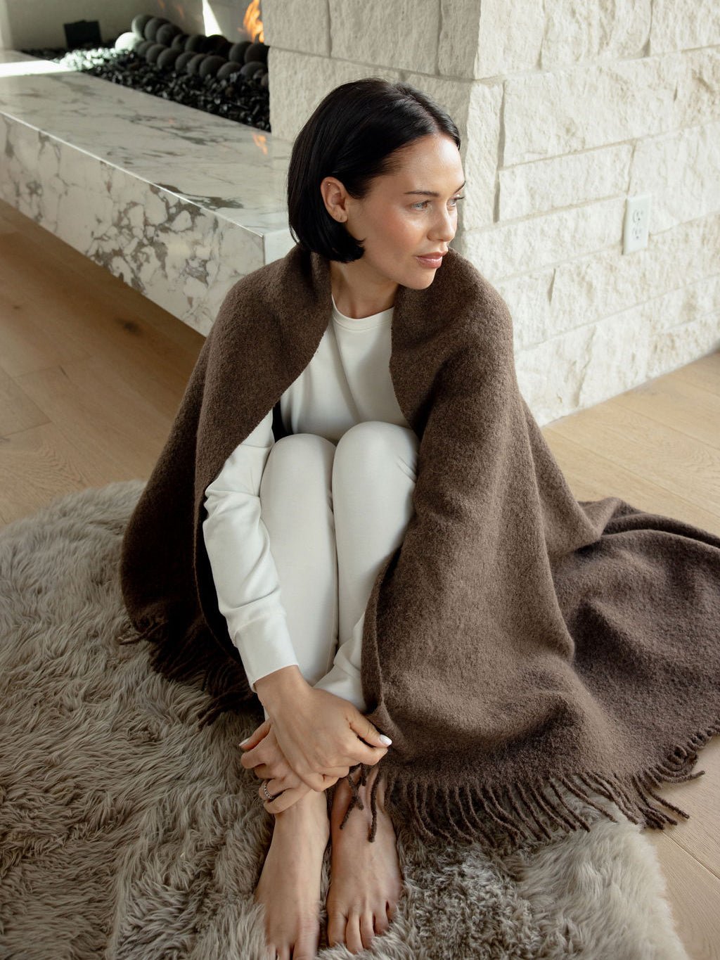 Woman sitting on the floor with the coffee boucle throw wrapped around her 