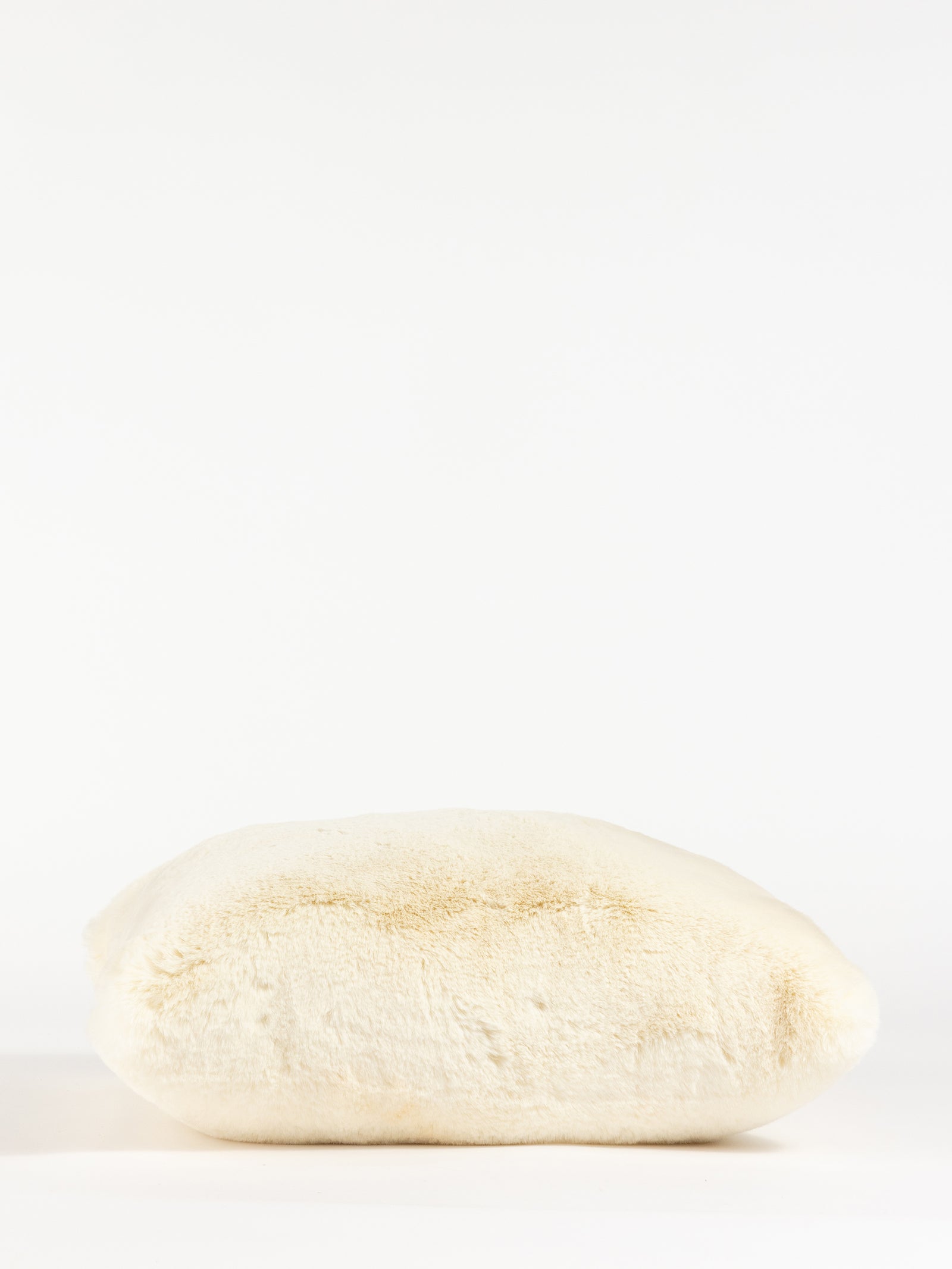 A Cuddle Pillow by Cozy Earth, featuring a plush off-white design and fluffy texture, is positioned against a plain white background. The pillow looks soft and inviting with gentle curves and a slightly uneven surface. 