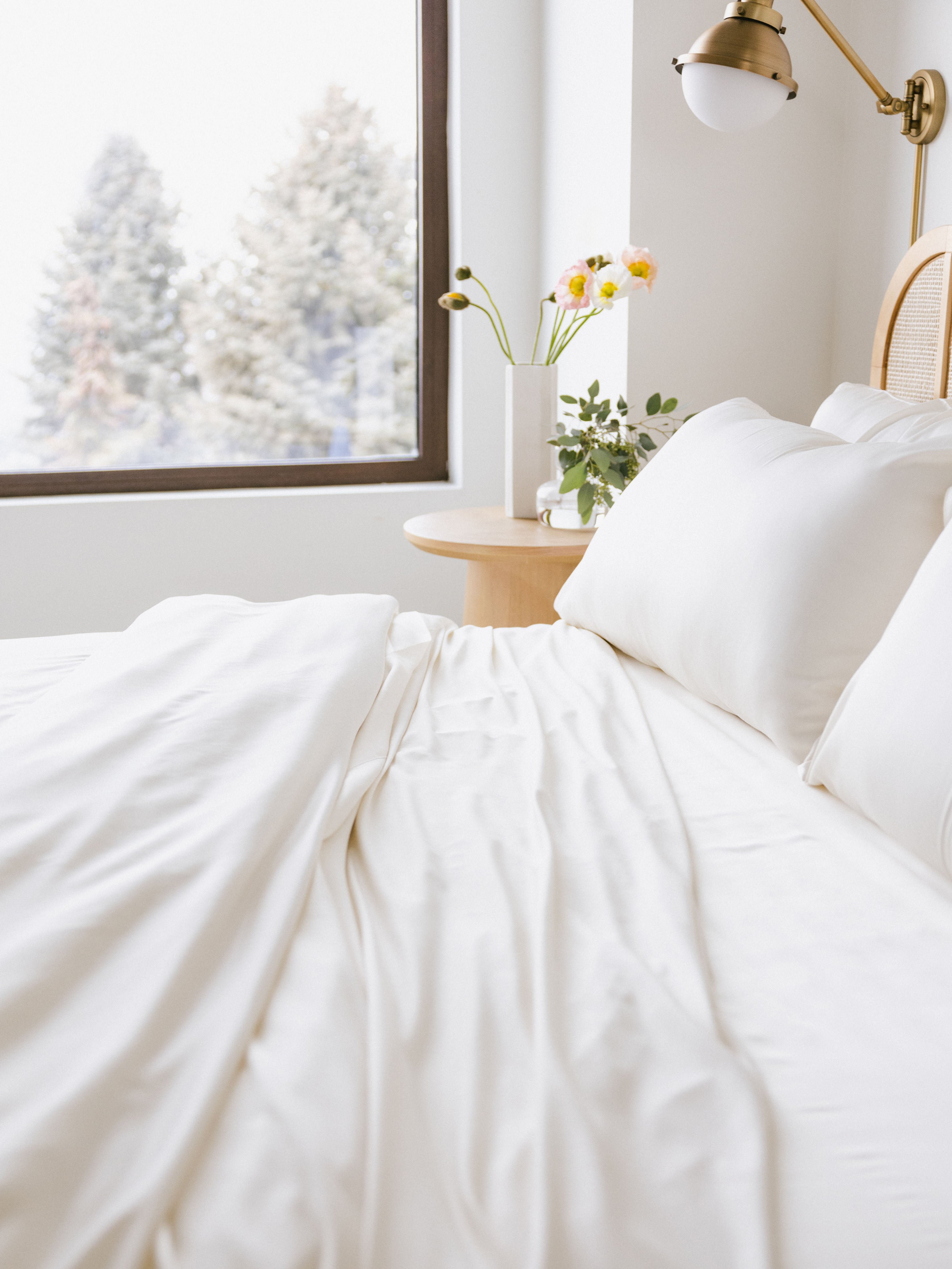 Creme bedding on an unmade bed with trees out the window 