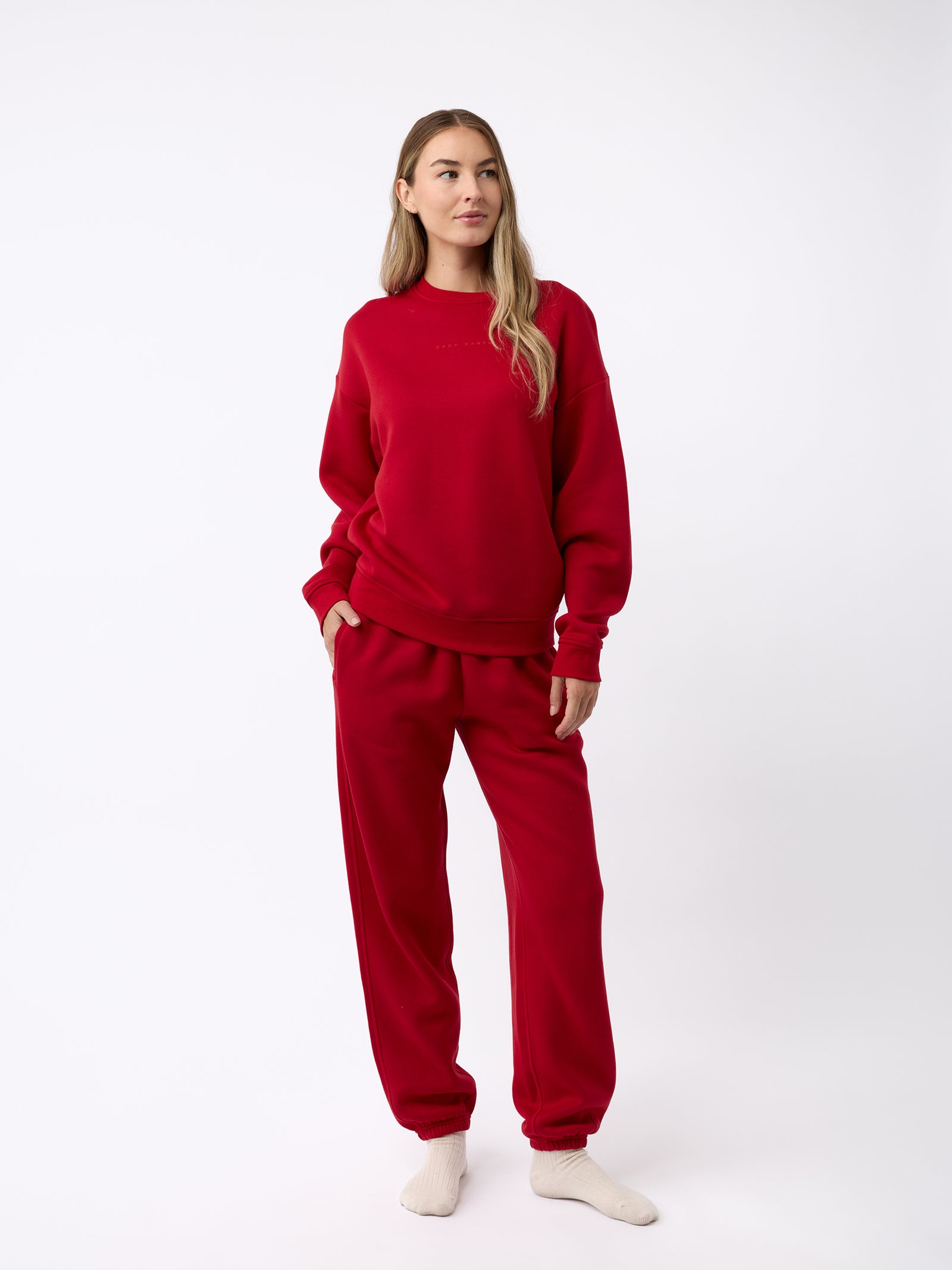 A person wearing the Women's CityScape Sweatpant by Cozy Earth, paired with a matching red sweatshirt, stands against a plain white background. They have long hair and are wearing white socks, creating a look that appears both comfortable and casual. 