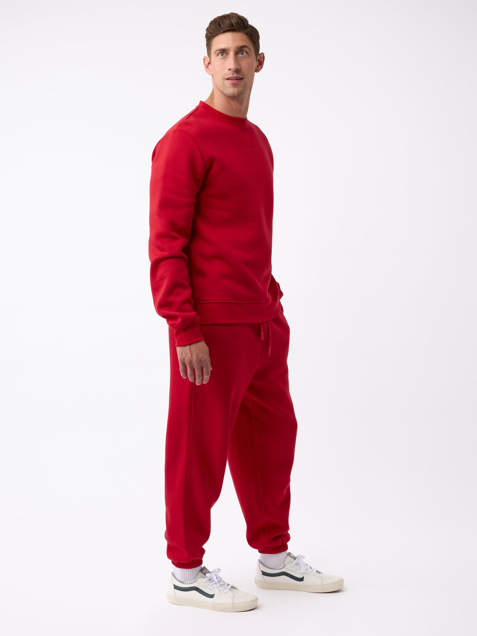 A person wearing the Men's CityScape Sweatpant by Cozy Earth along with a matching red sweatshirt stands against a plain white background. They are gazing slightly to the right and have white sneakers on. 