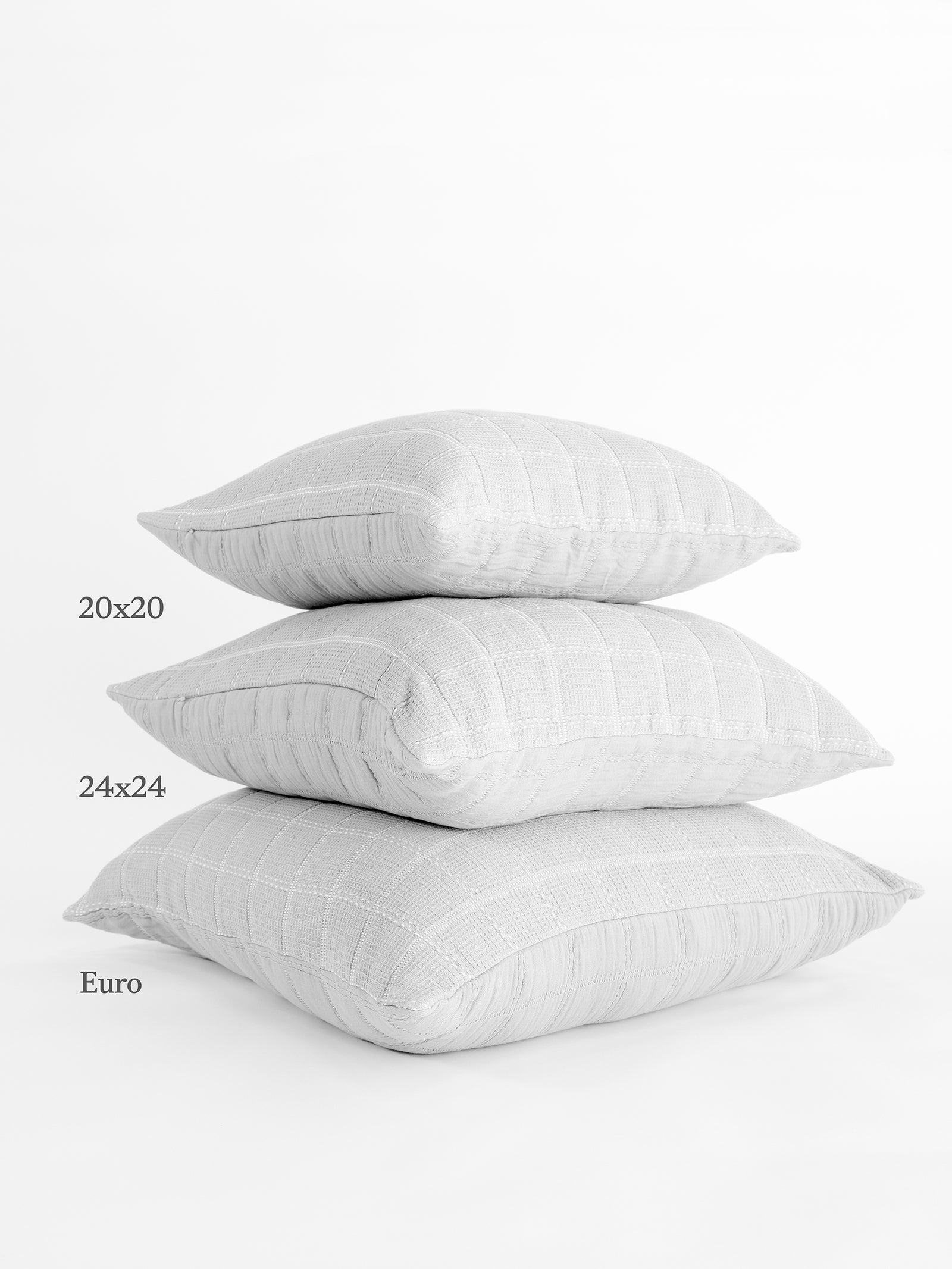 A stack of three Cozy Earth Waffle Windowpane Pillows in light grey is shown against a plain white background. The pillows, labeled from top to bottom, come in sizes 20x20, 24x24, and Euro, each featuring a subtle checkered pattern. 