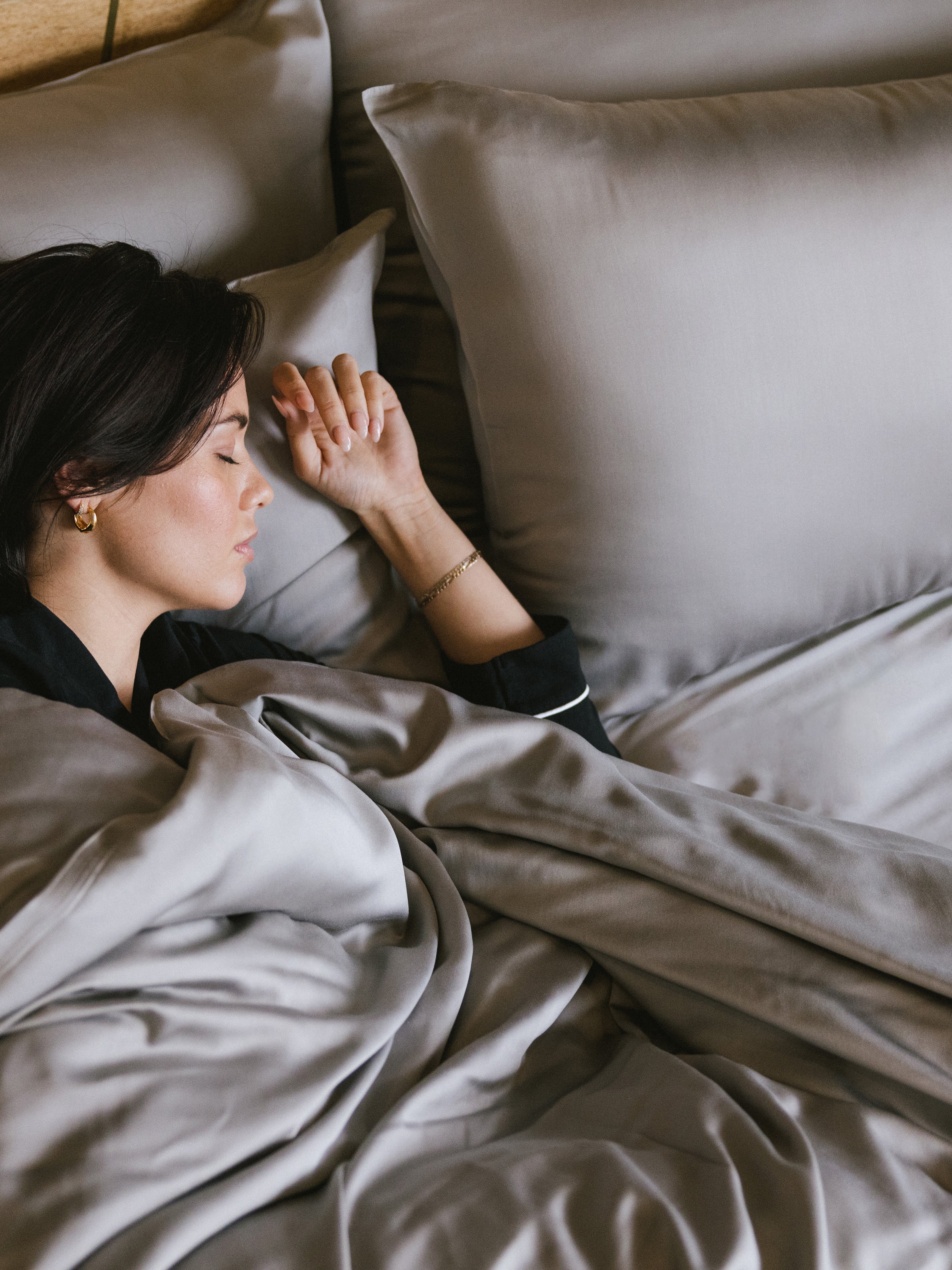 Woman sleeping in bed with dove grey bedding 
