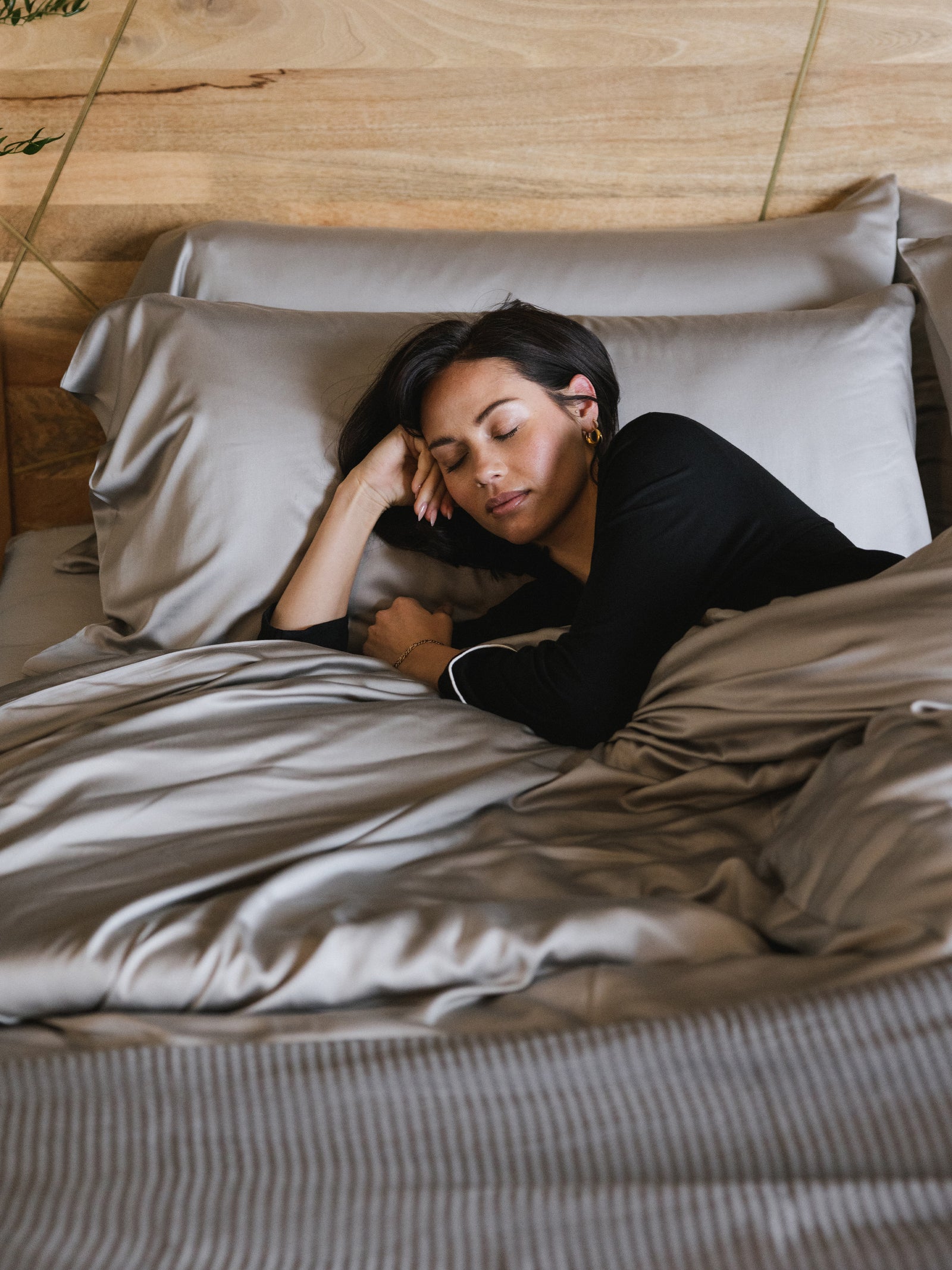 Woman with her arm up sleeping in bed with dove grey sheets 